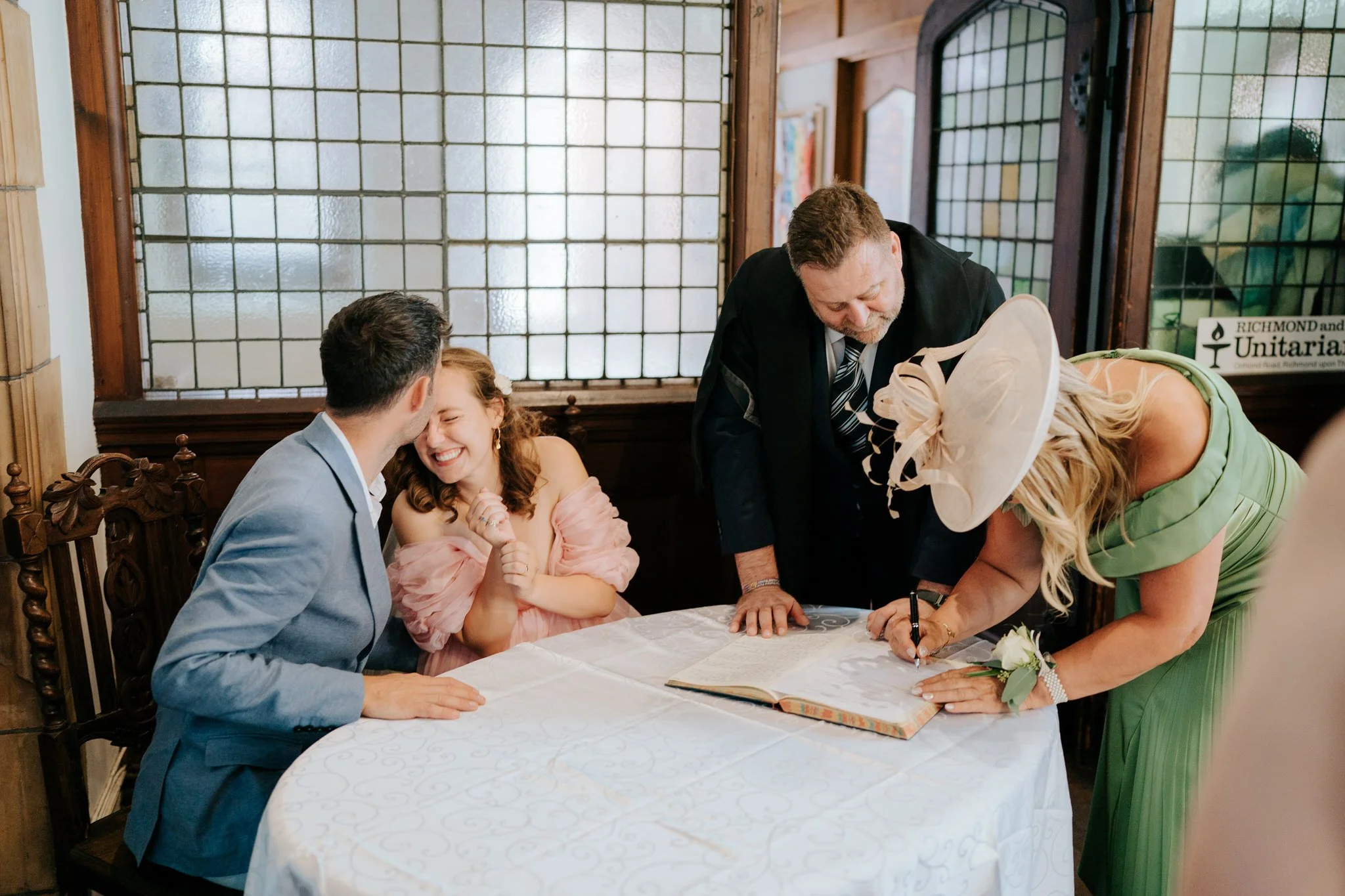 Groom kisses his bride on the forehead as one of the witnesses signs the register during ceremony at Richmond and Putney Unitarian church