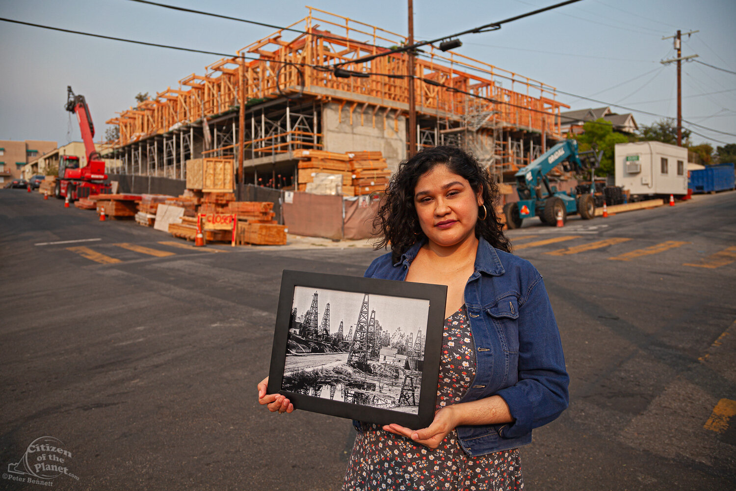  Resident and activist Brenda Valdivia, who has suffered from lifelong health conditions that she attributes to the wells, stands in front of the 120-unit development by Aragon Holdings. She holds a photo circa 1895-1901 of that area. 