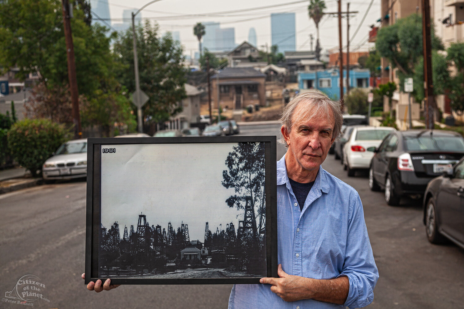  Resident Thomas Gustafson holds a photo from 1901 in front of an original home on Edgeware Road and Court Street, once surrounded by oil derricks.  