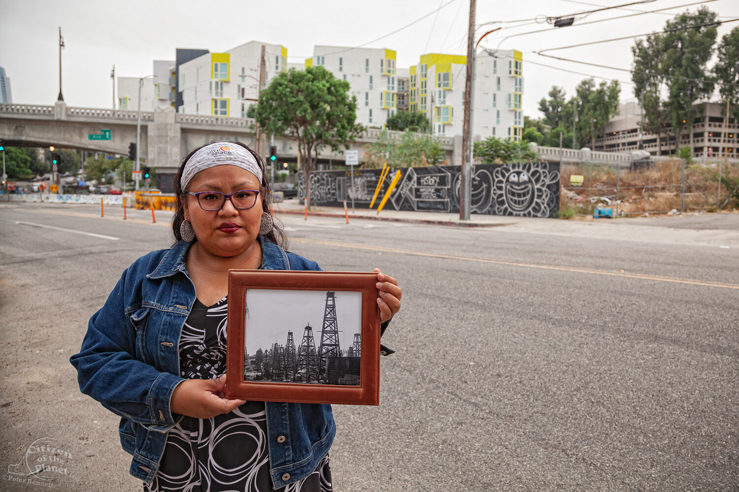  Resident, Esther Salas stands in front of the future site of the Echo Park Hotel, on W. 1st Street and Glendale Boulevard, a 185-room hotel. She holds a 1901 photo of the area, showing oil derricks lining the road.  