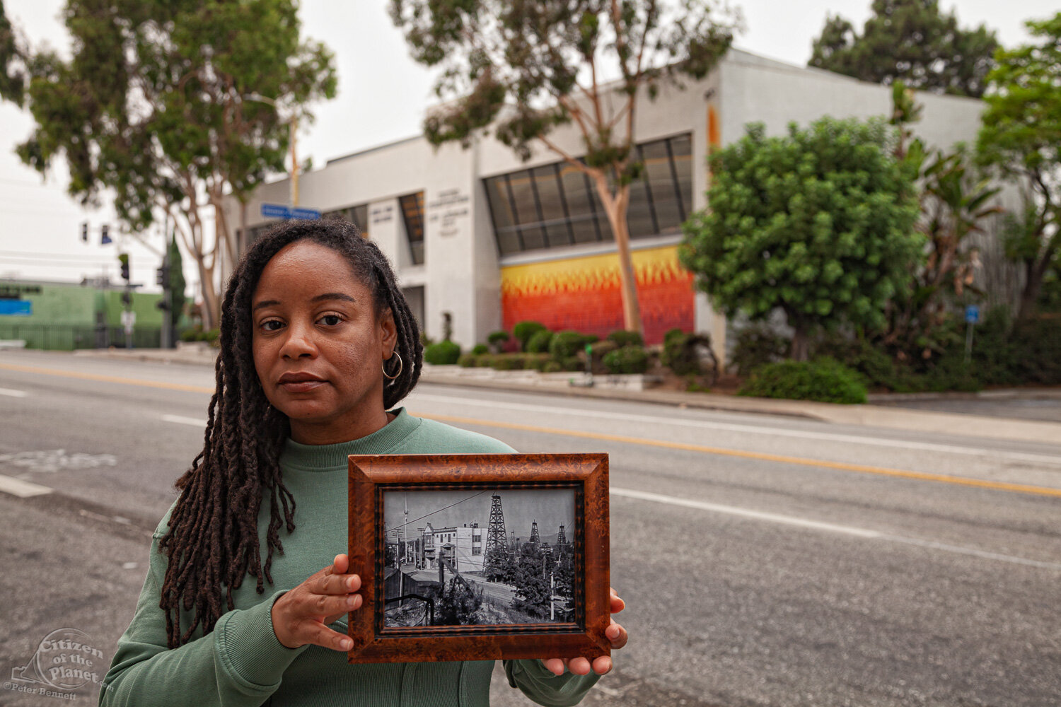  Resident, Mercedes Yolanda Cooper holds a 1905 photo of the intersection of W. 1st Street and Belmont Ave. Today, though not visible, the oil wells lie shallowly below the ground.  