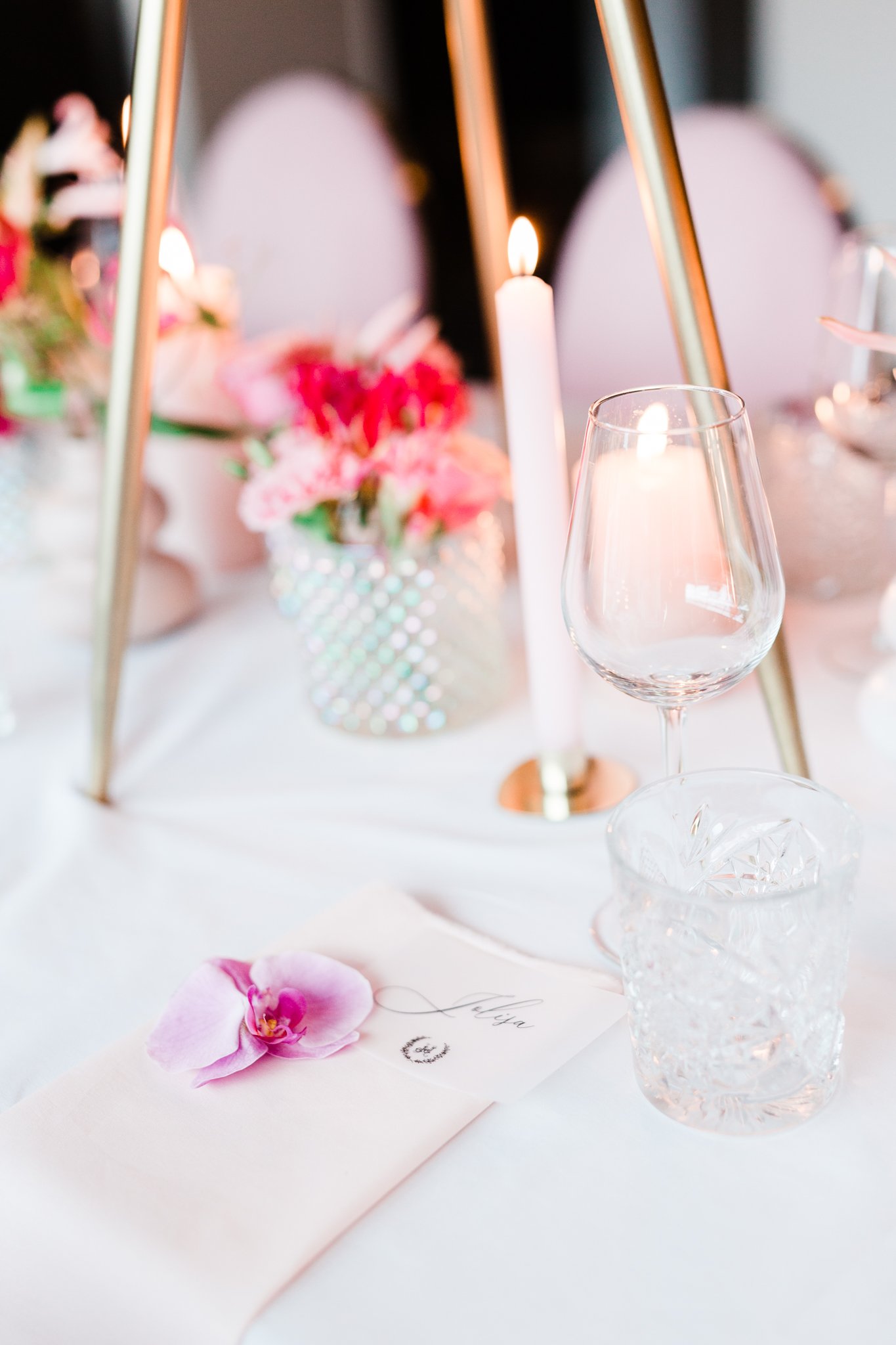 Elegante tafelopstelling met kaarsen, glazen, bloemen en een servet met orchidee.