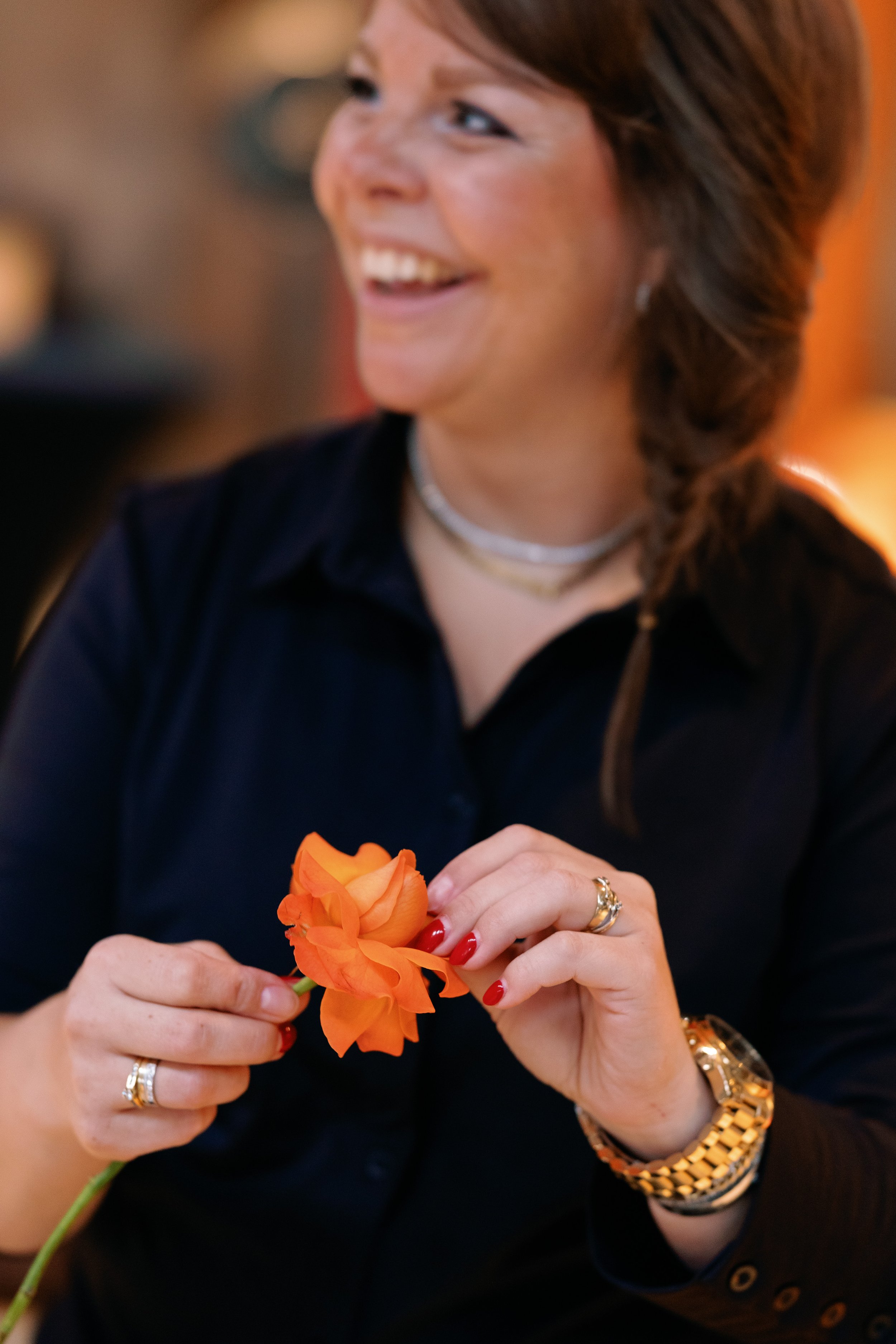 Vrouw met glimlach houdt een oranje roos vast.