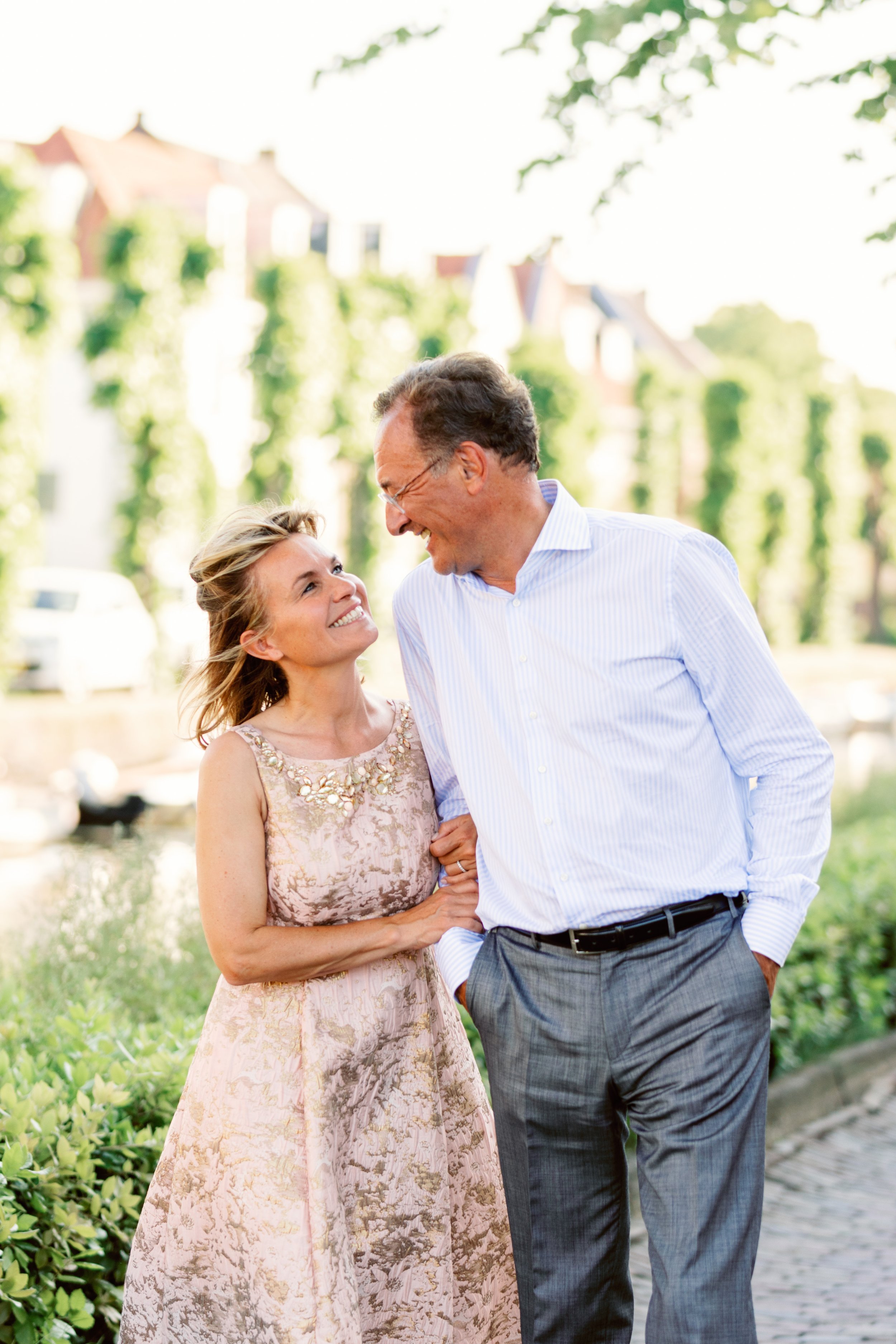Twee lachende mensen, een vrouw in een mooie jurk en een man in een overhemd, arm in arm op een zonnige dag.