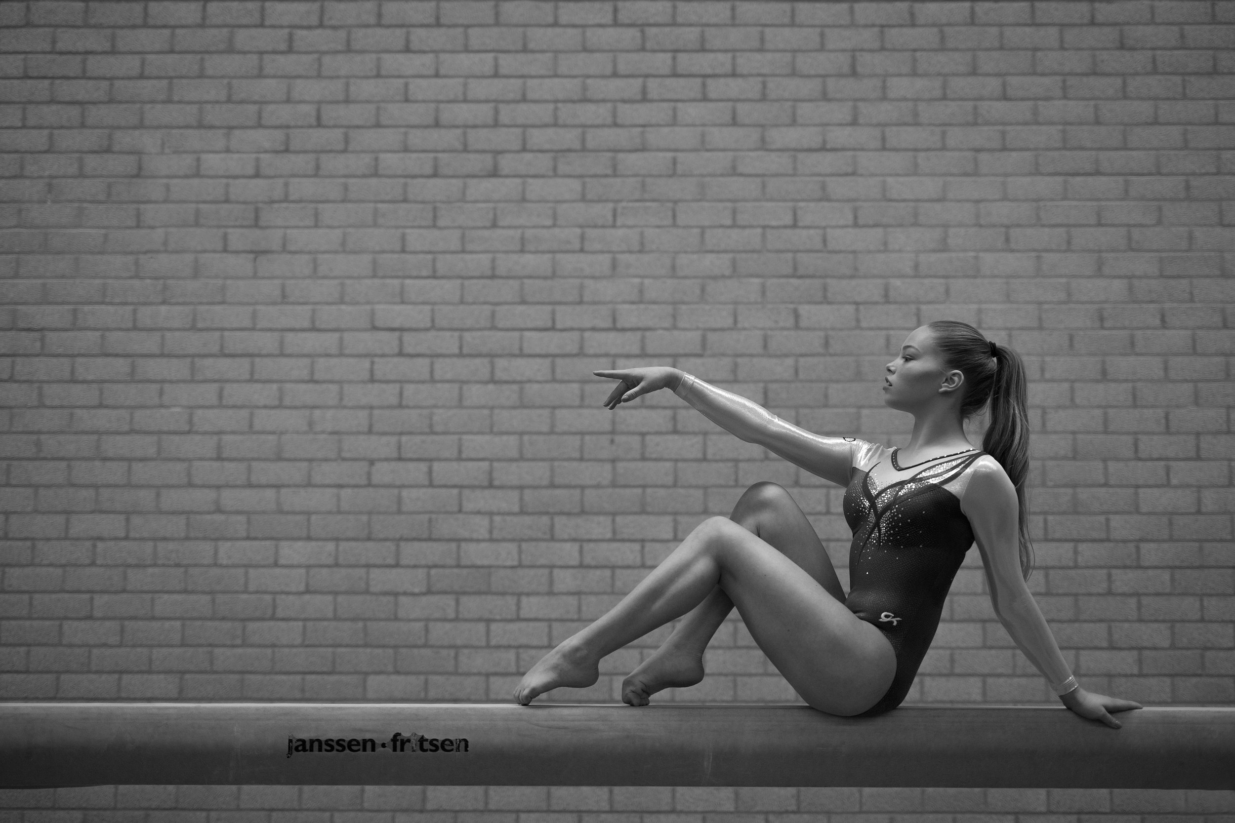 Gymnast op evenwichtsbalk tegen een bakstenen muur.