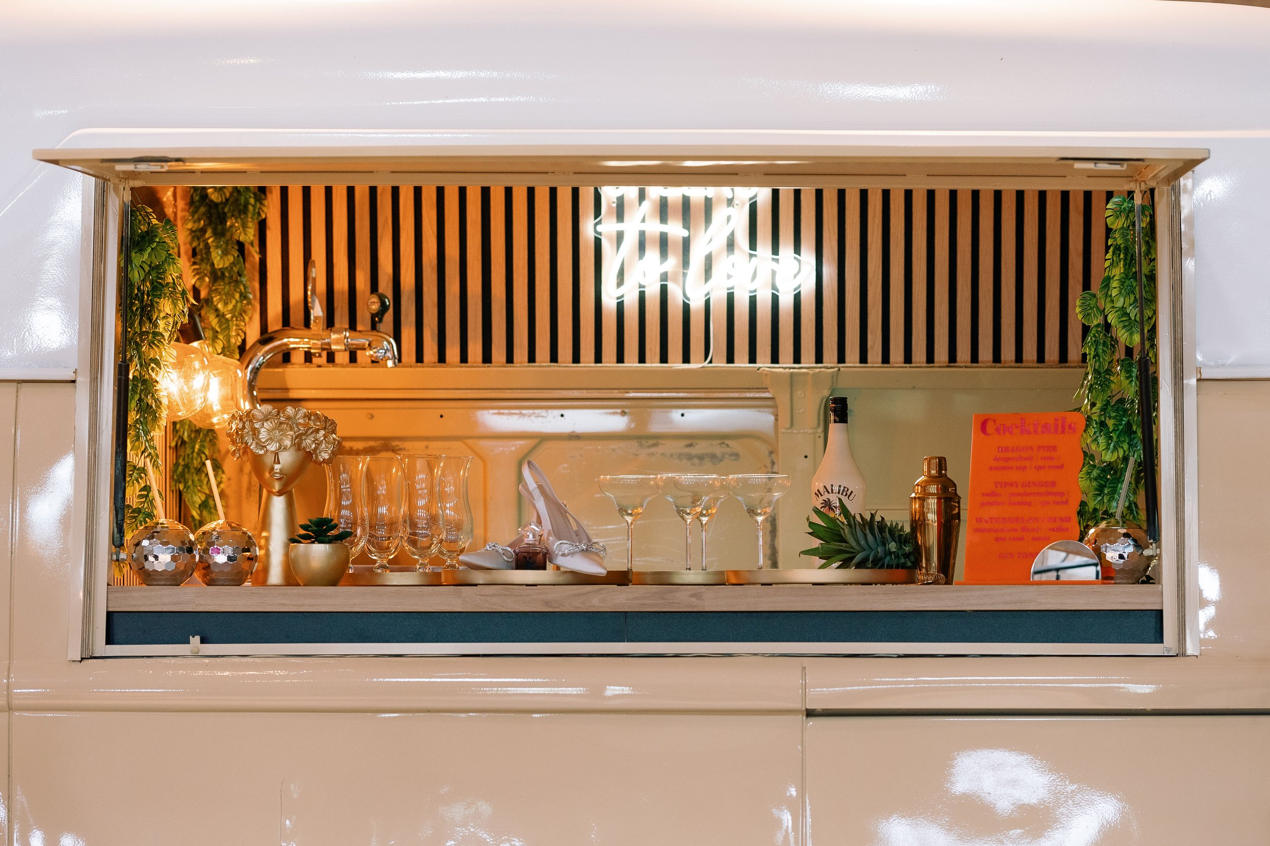 Een mobiele bar met glazen, een fles Malibu, en een cocktailmenu.