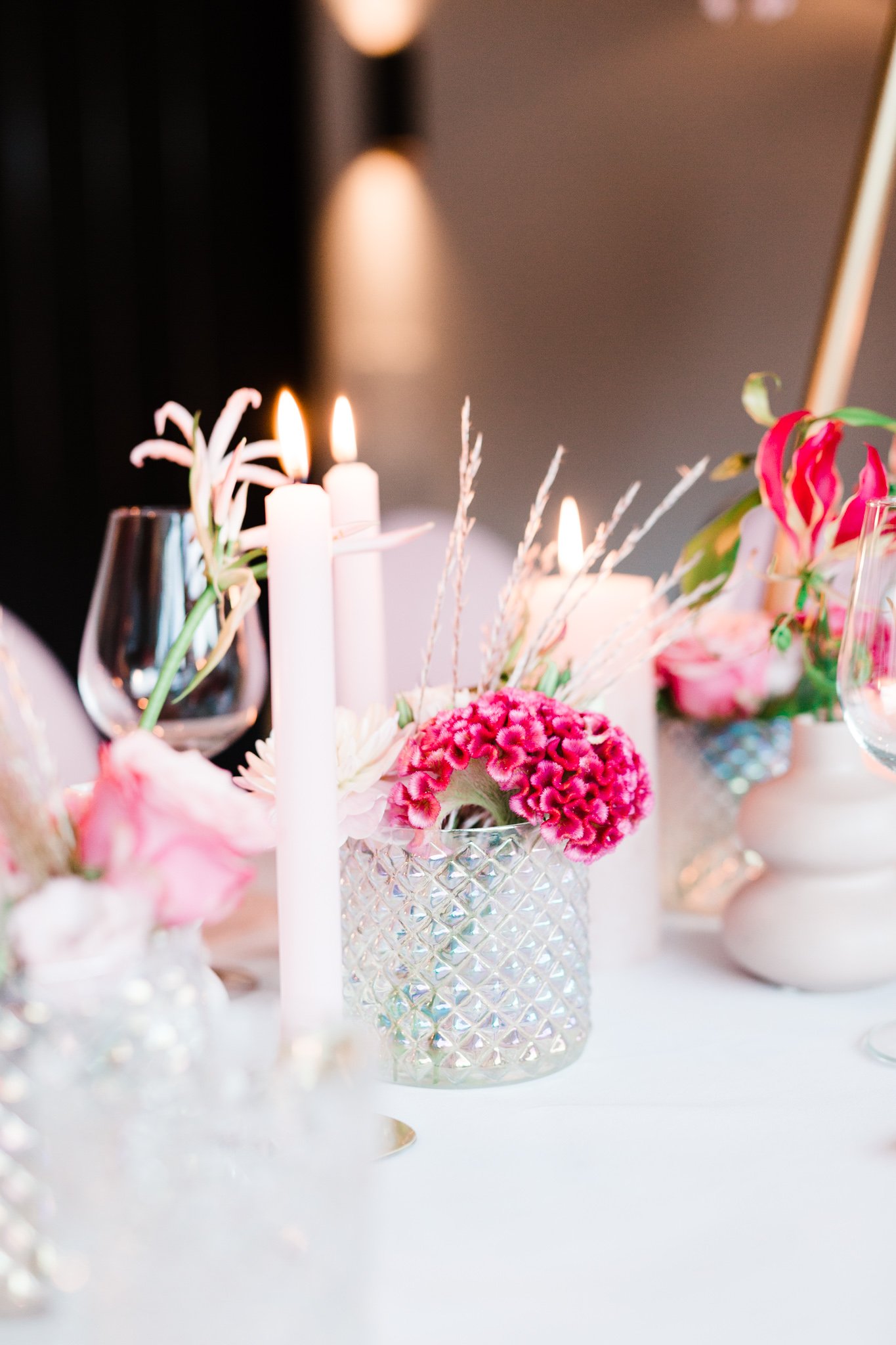 Gedekte tafel met brandende kaarsen, bloemen in glazen vazen, en wijnglazen.