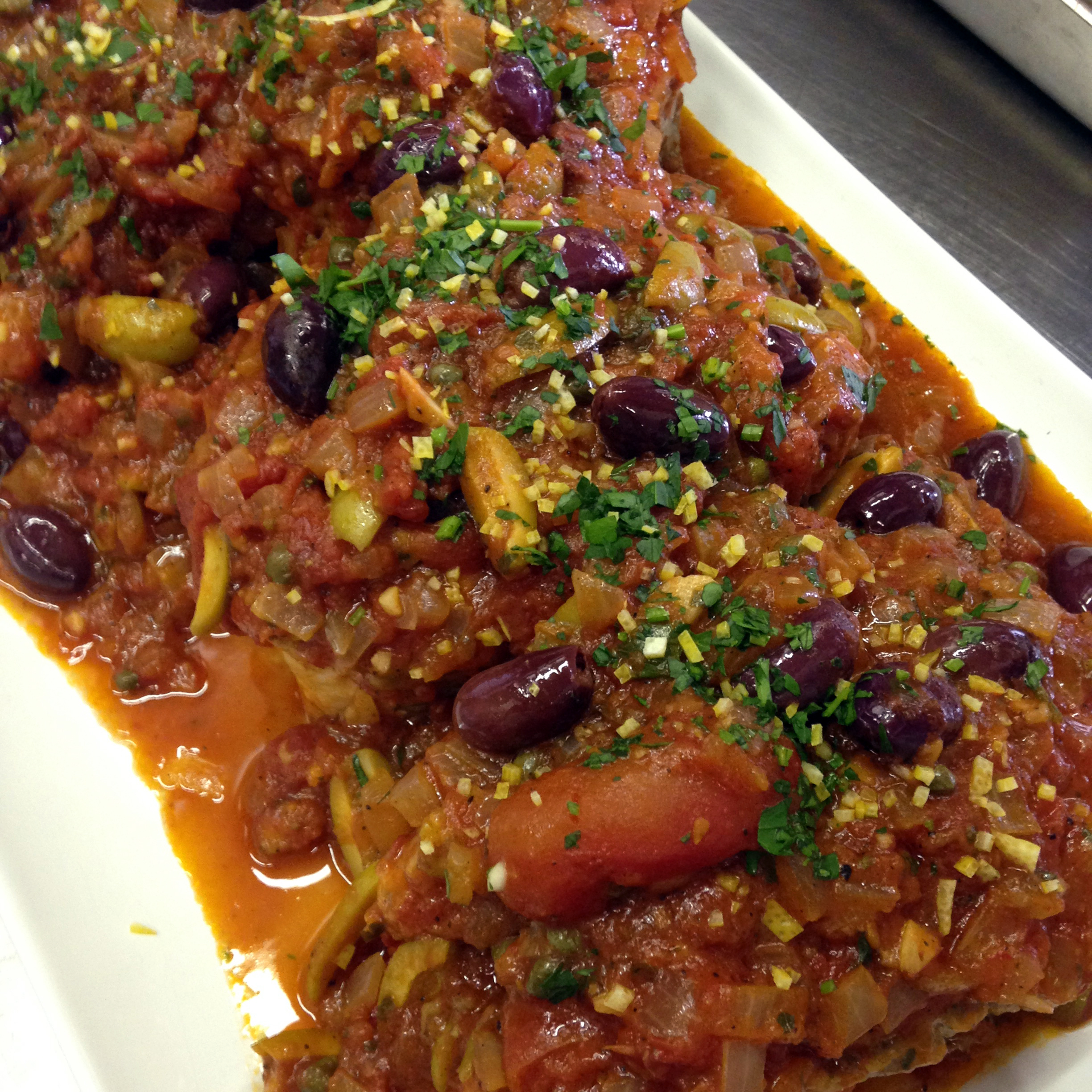 Steaks of striped bass are hidden under a blanket of spicy puttanesca sauce