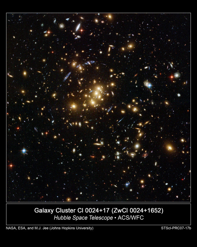 The rich galaxy cluster Cl 0024+17. Blue streaks near the centre are smeared images of very distant background galaxies. Their light is being bent and magnified by the intervening cluster, in an effect called gravitational lensing.