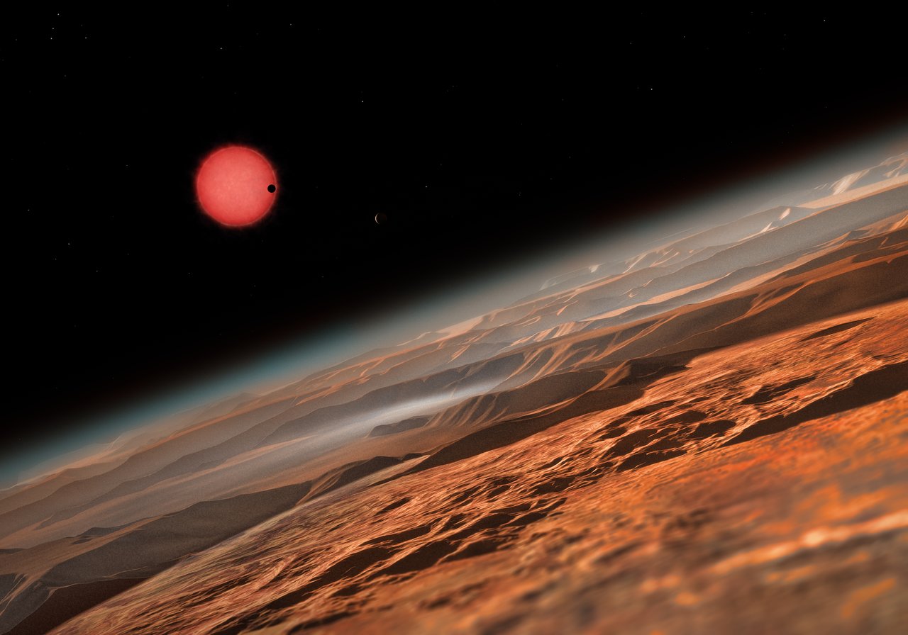 This artist’s impression shows an imagined view from close to one of the three planets orbiting an ultracool dwarf star just 40 light-years from Earth that were discovered using the TRAPPIST telescope at ESO’s La Silla Observatory. These worlds have sizes and temperatures similar to those of Venus and Earth and are the best targets found so far for the search for life outside the Solar System. They are the first planets ever discovered around such a tiny and dim star. In this view one of the inner planets is seen in transit across the disc of its tiny and dim parent star. Image Credit: ESO/M. Kornmesser