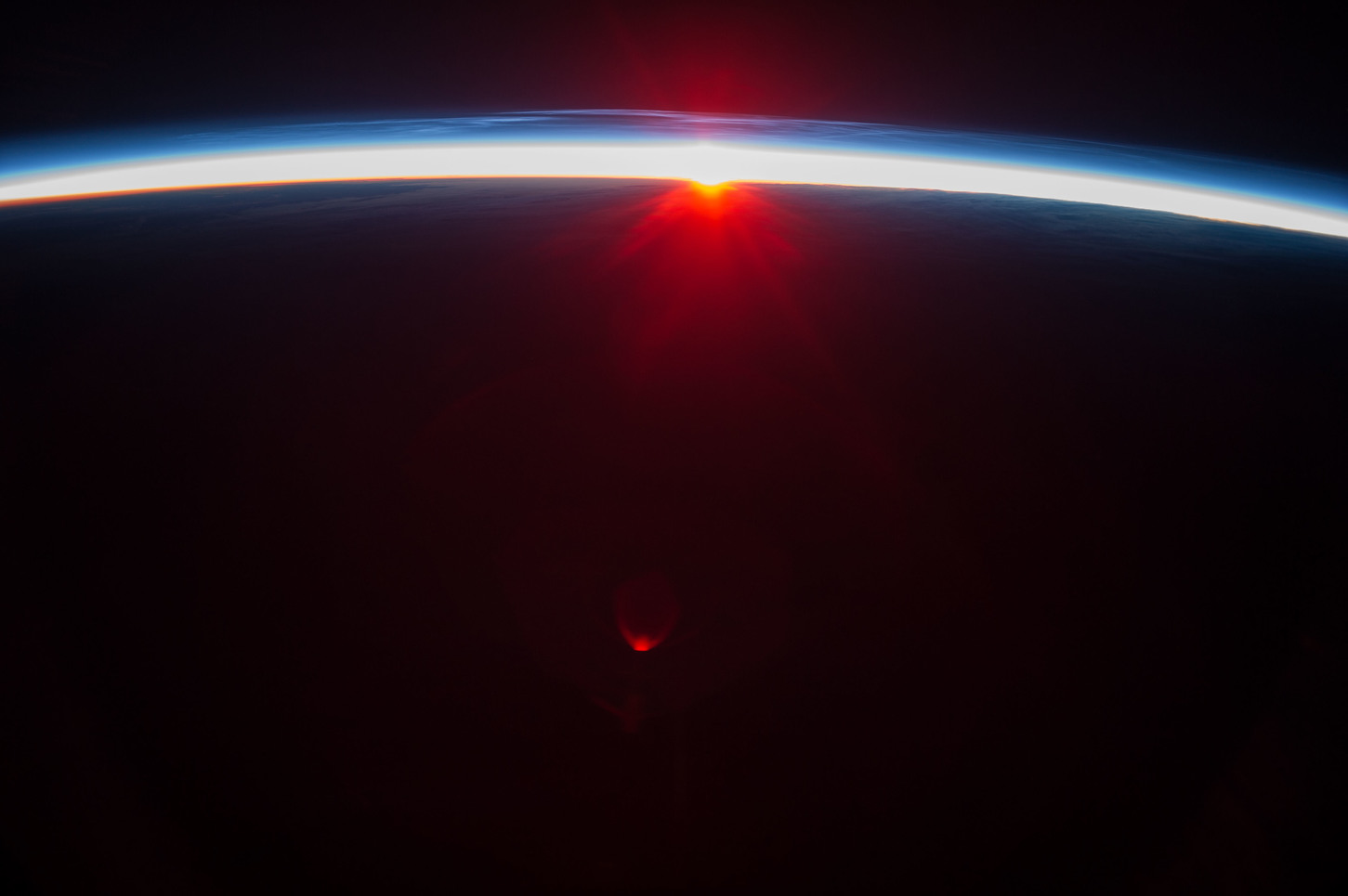 Photo taken by astronauts of noctilucent clouds in Earth’s atmosphere above the midnight sun (above the blue layer). - Image Credit: NASA