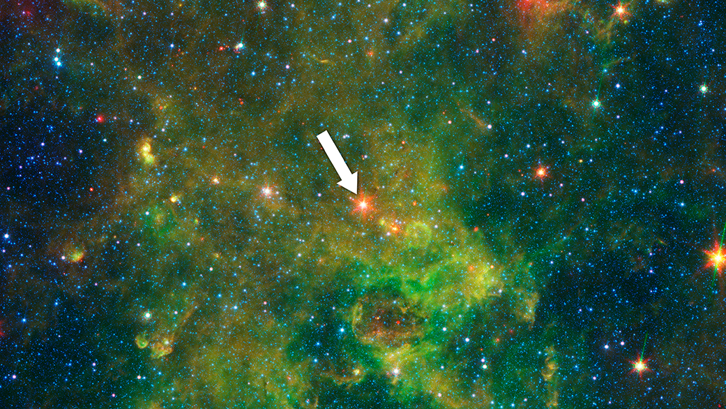An age-defying star designated as IRAS 19312+1950 (arrow) exhibits features characteristic of a very young star and a very old star. The object stands out as extremely bright inside a large, chemically rich cloud of material, as shown in this image from NASA’s Spitzer Space Telescope. A NASA-led team of scientists thinks the star – which is about 10 times as massive as our sun and emits about 20,000 times as much energy – is a newly forming protostar. That was a big surprise because the region had not been known as a stellar nursery before. But the presence of a nearby interstellar bubble, which indicates the presence of a recently formed massive star, also supports this idea. – Image Credits: NASA/JPL-Caltech