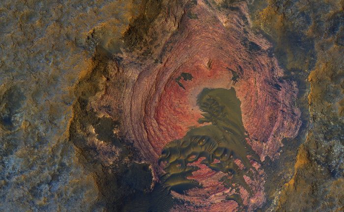 This colorful image of Martian bedrock, punctuated in the center by dunes, is courtesy of the HiRise camera aboard NASA's Mars Reconnaissance Orbiter. - Image Credit: NASA/JPL/University of Arizona