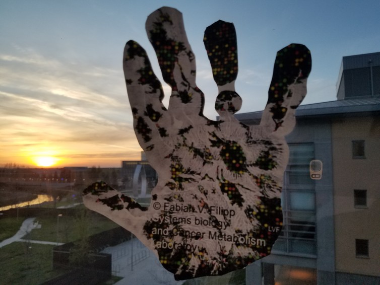 Artistic illustration of an epigenomic handprint capturing regulation of a person beyond changes in DNA. In background research campus with art statue ‘New Beginnings,’ symbolizing hope for cure. - Image Credit: Systems Biology and Cancer Metabolism Laboratory, Fabian V. Filipp