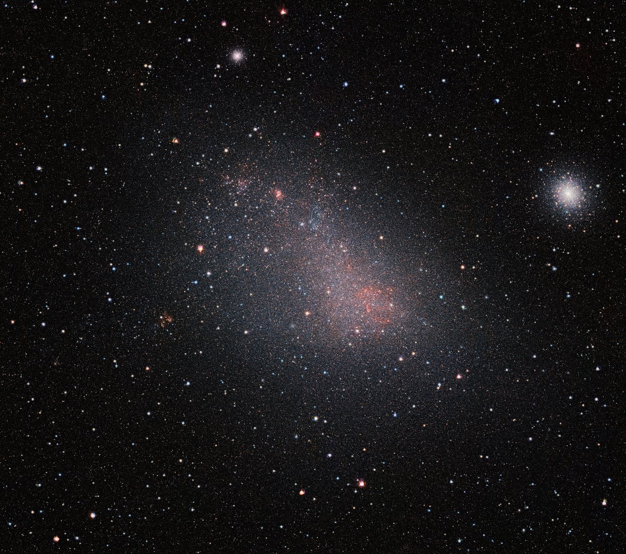 The Small Magellanic Cloud (SMC) galaxy is a striking feature of the southern sky even to the unaided eye. But visible-light telescopes cannot get a really clear view of what is in the galaxy because of obscuring clouds of interstellar dust. VISTA’s infrared capabilities have now allowed astronomers to see the myriad of stars in this neighbouring galaxy much more clearly than ever before. The result is this record-breaking image — the biggest infrared image ever taken of the Small Magellanic Cloud — with the whole frame filled with millions of stars. As well as the SMC itself this very wide-field image reveals many background galaxies and several star clusters, including the very bright 47 Tucanae globular cluster at the right of the picture. - Image Credit: ESO/VISTA VMC