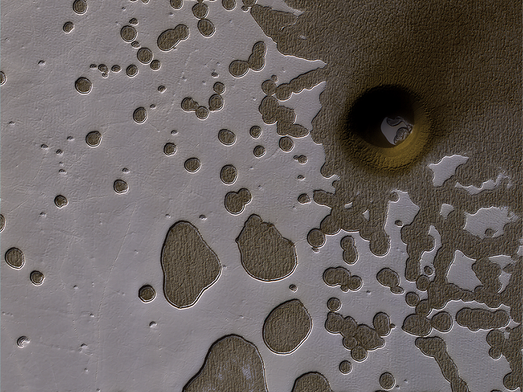 The HiRISE camera on NASA's Mars Reconnaissance Orbiter captured this unusual crater or pit on the surface of Mars. Frozen carbon dioxide gives the region its unique "Swiss cheese" like appearance. - Image Credit: NASA/JPL/University of Arizona