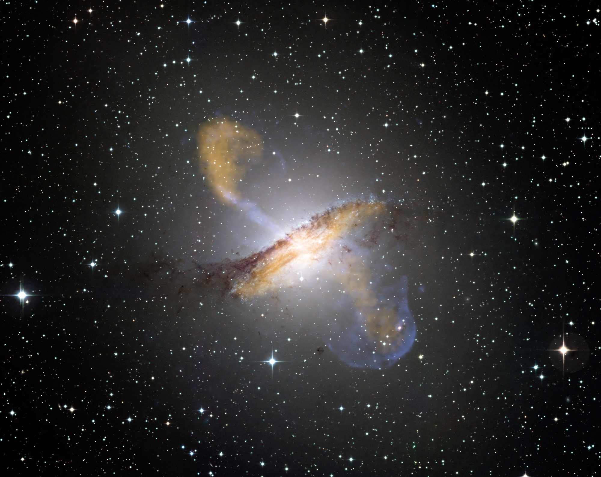 Colour composite image of Centaurus A, revealing the lobes and jets emanating from the active galaxy’s central black hole. - Image Credit: ESO/NASA/CXC/CfA/WFI/MPIfR/APEX/A.Weiss et al./R.Kraft et al.