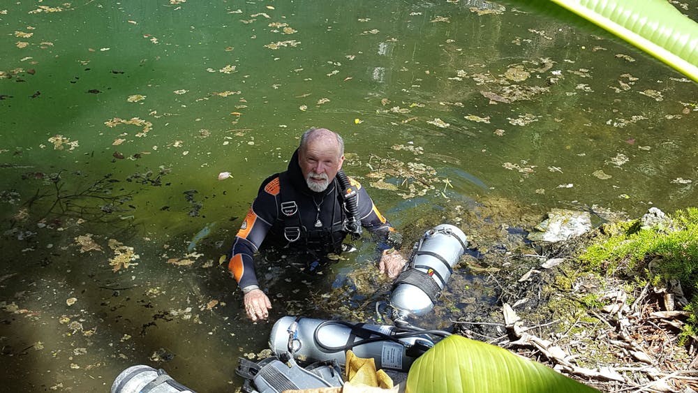 Tom Iliffe preparing for a side mount dive at Cliff Pool, Bermuda. Rather than carrying tanks on his back as in conventional scuba, a tank is clipped off under each arm, allowing him to pass through low sections in a cave where it would otherwise be impossible to go. - Image Credit: Gil Nolan, CC BY-ND
