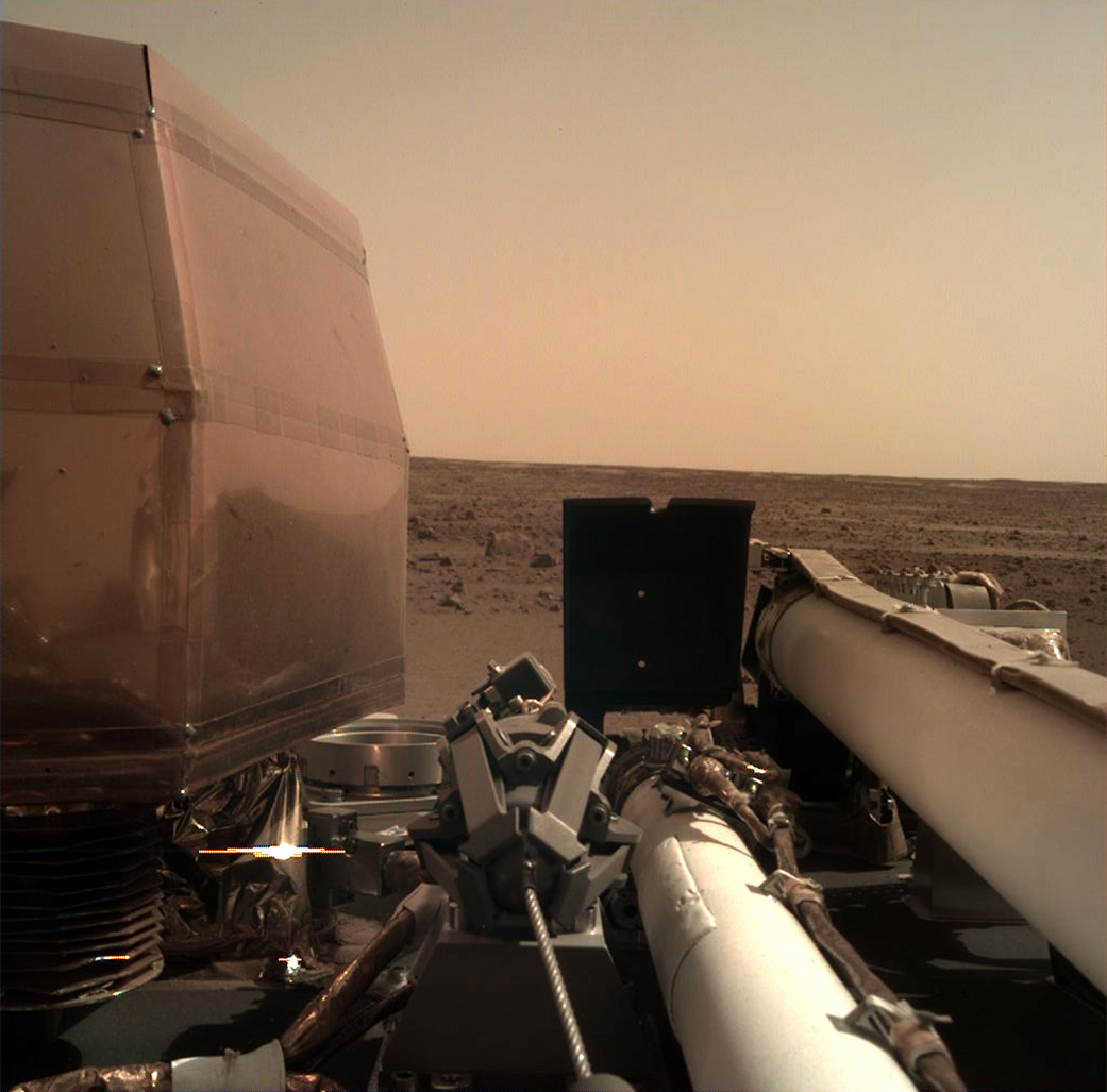 The Instrument Deployment Camera (IDC), located on the robotic arm of NASA's InSight lander, took this picture of the Martian surface on Nov. 26, 2018, the same day the spacecraft touched down on the Red Planet. The camera's transparent dust cover is still on in this image, to prevent particulates kicked up during landing from settling on the camera's lens. This image was relayed from InSight to Earth via NASA's Odyssey spacecraft, currently orbiting Mars. - Image Credits: NASA/JPL-Caltech