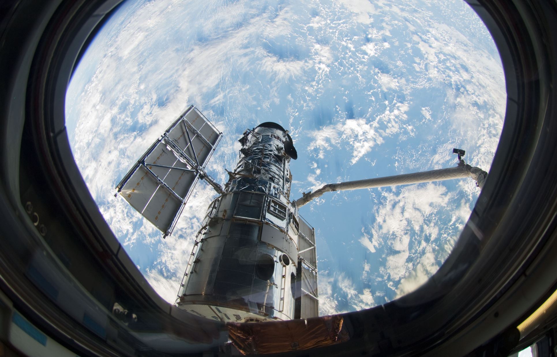 A window on the space shuttle Atlantis frames Hubble as astronaut Megan McArthur uses the shuttle's robot arm to grab the telescope in preparation for the final servicing mission. From its perch 340 miles above Earth, the famed space telescope has t…