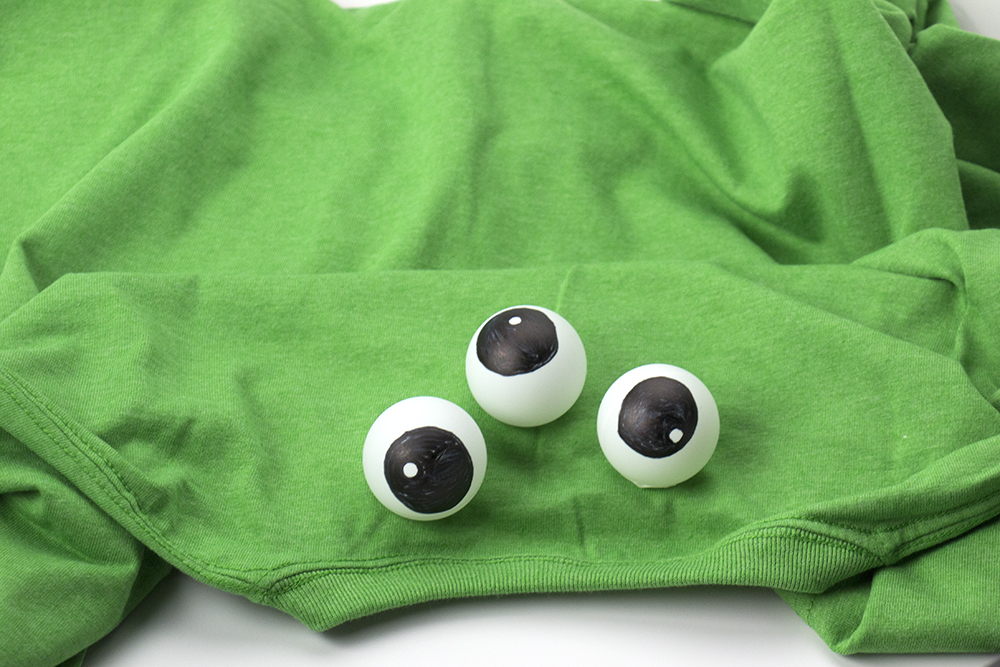 Peel off the split liner, exposing the other side of the double sided Fearless Dot. Then place the sticky-side down on the shirt. Repeat for all three eyes. That’s it! Your silly monster costume is ready. Have your silly little monster put on the shirt without putting their head through the neck hole. 