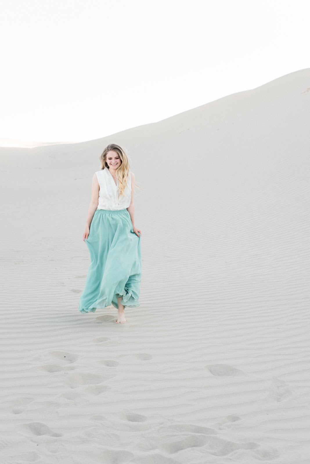 Zoomed out photo of woman smiling and walking through sand dune