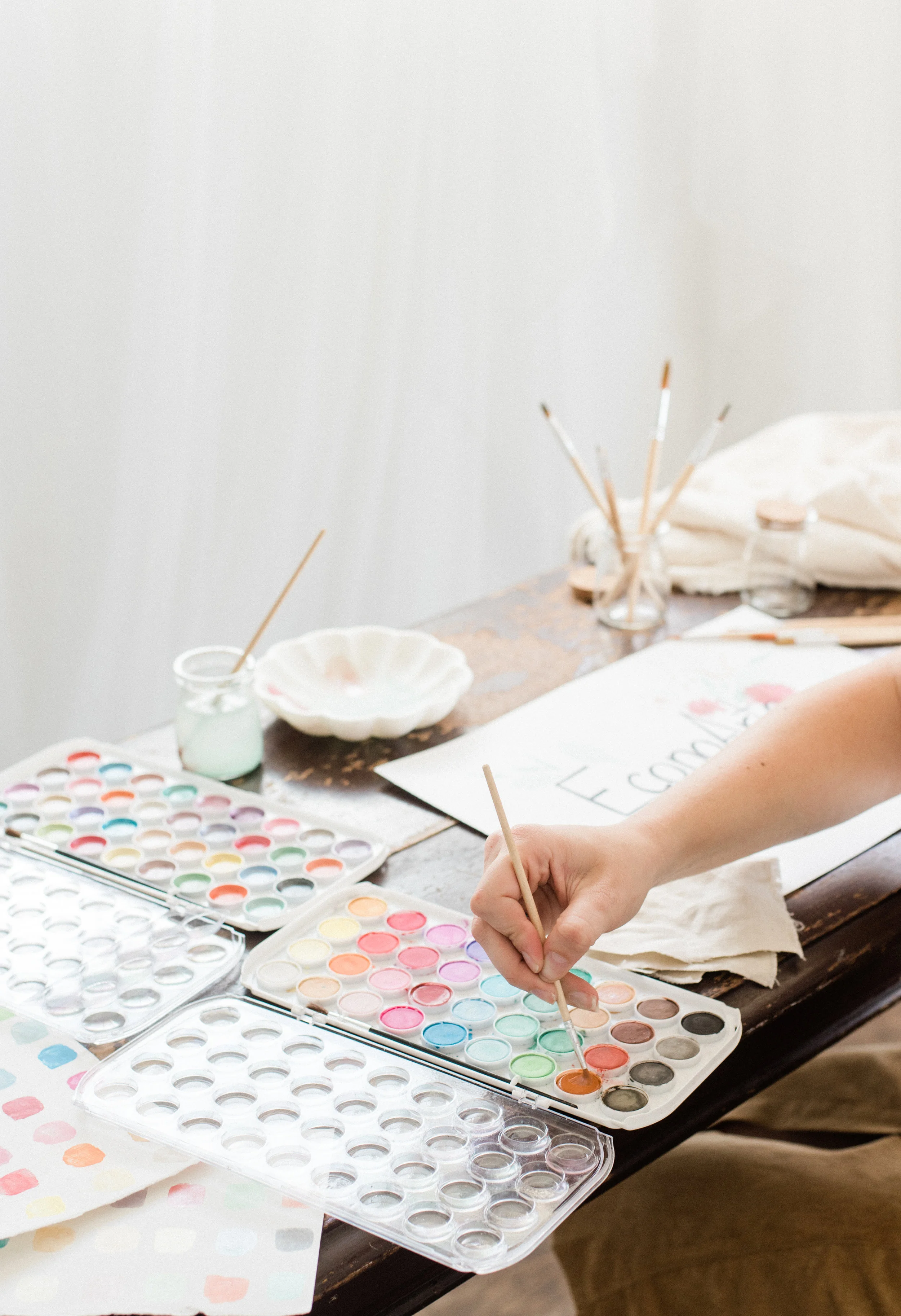 A paintbrush is dipped in a palette tray full of paint