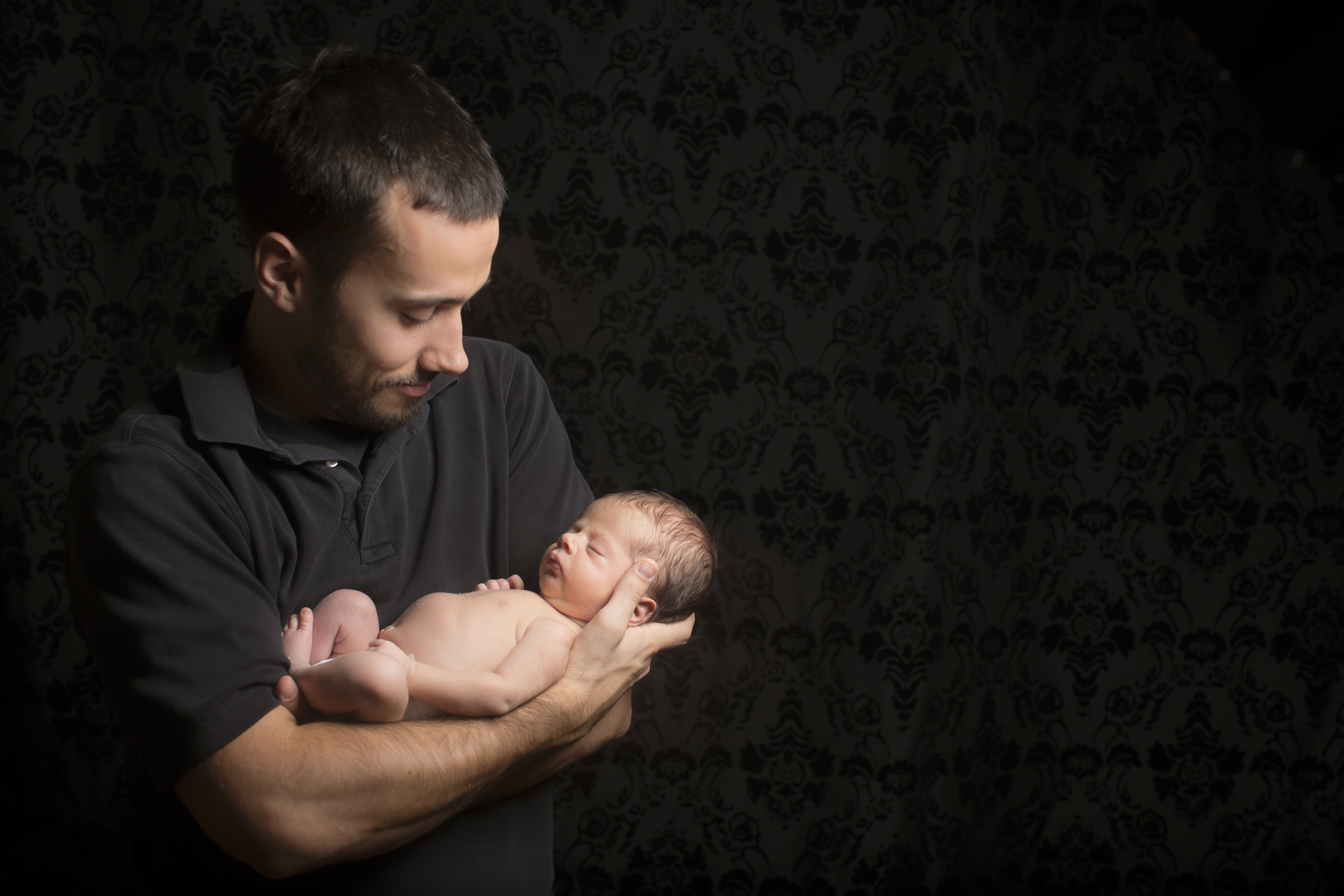 48 modern father cradling son newborn photography on black studio session.jpg