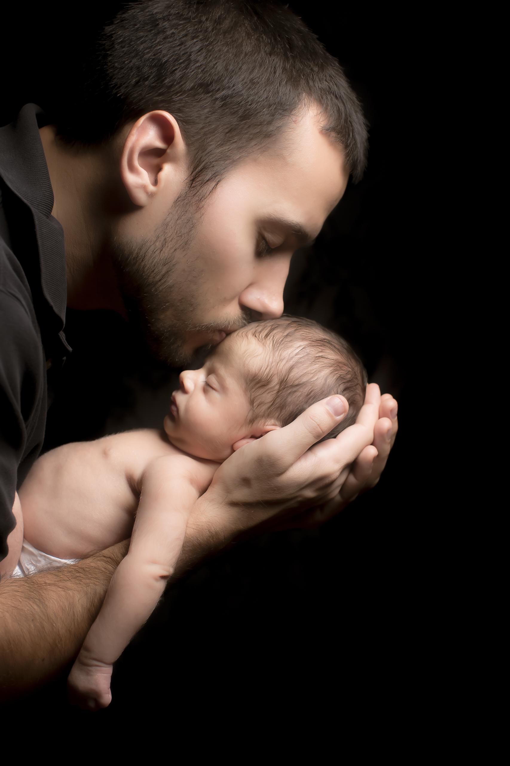 50 modern father kissing son newborn photography on black studio session.jpg