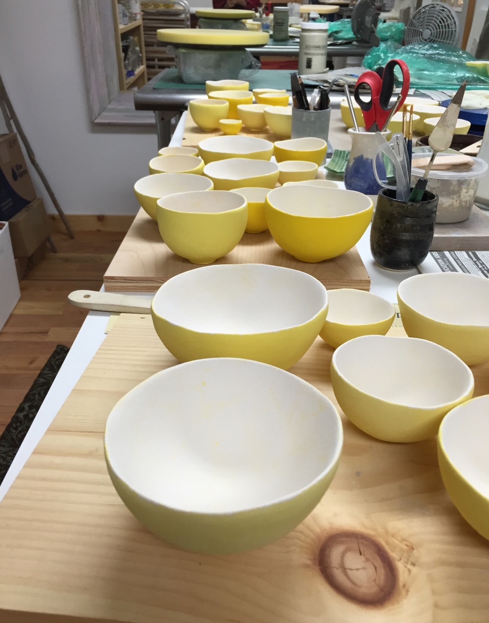 Bowls being glazed. Each group is glazed in different shades of yellow.