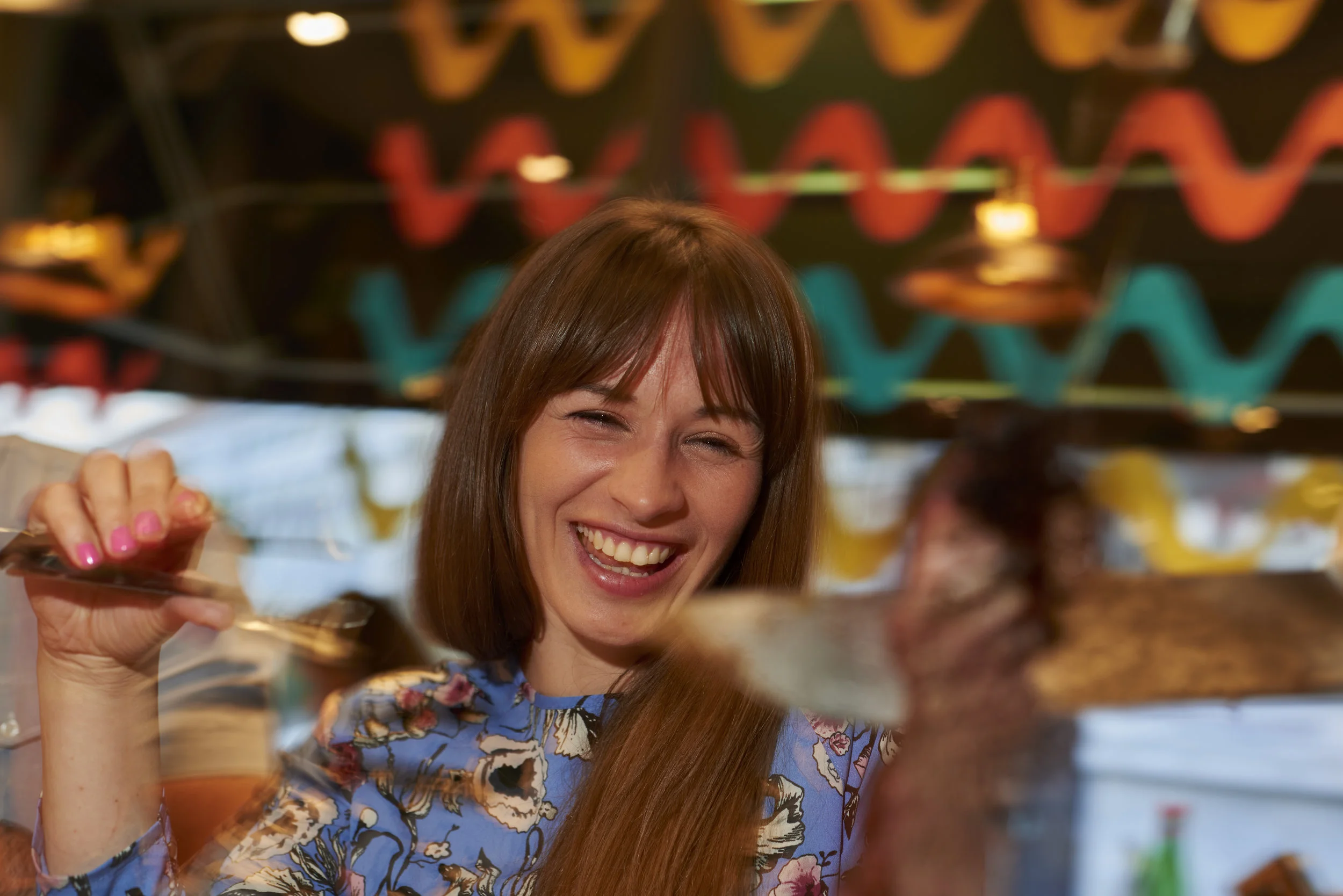 Woman laughing in a restaurant as she’s being served her meal in a lively and colourful environment