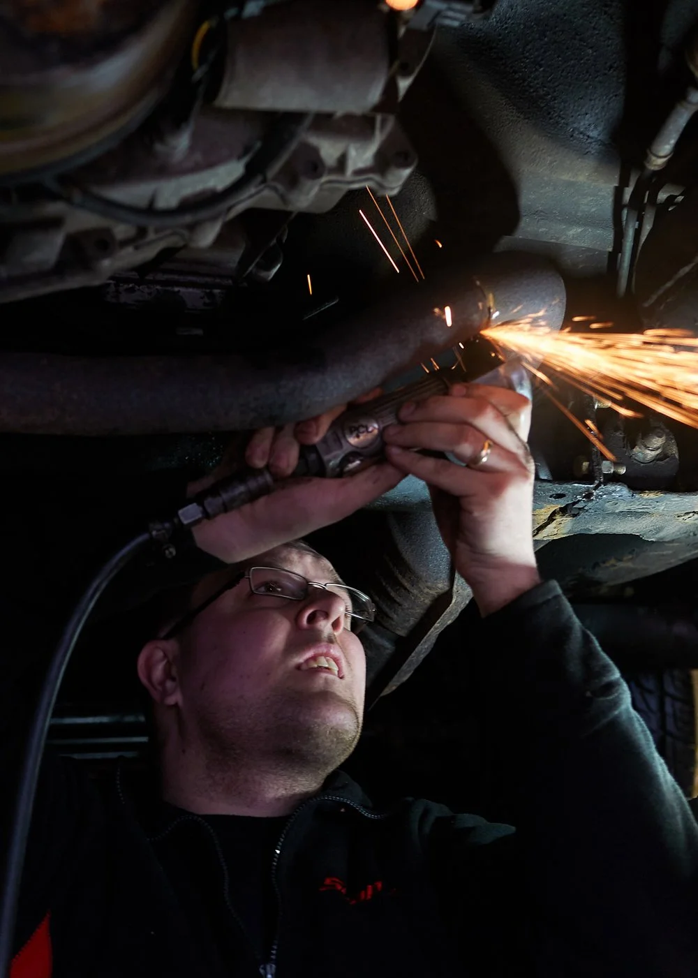 Portrait of a Mechanic at work using an angle grinder creating fiery sparks under the chassis of a car