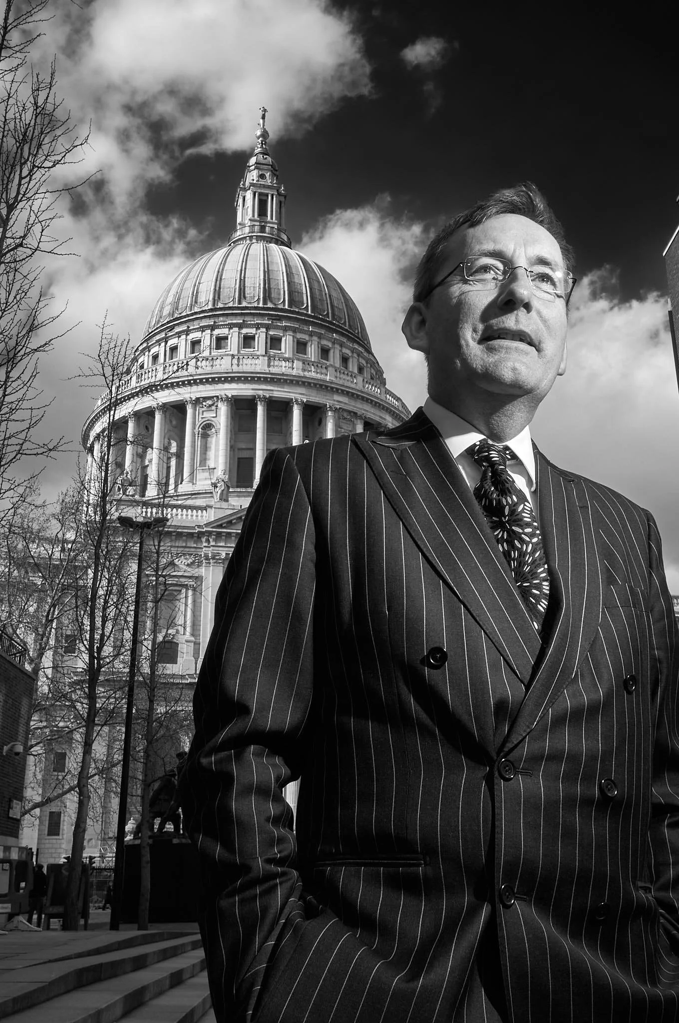 Black and white portrait of a man wearing a pin stripe suit standing in front of St. Paul’s Cathedral in London