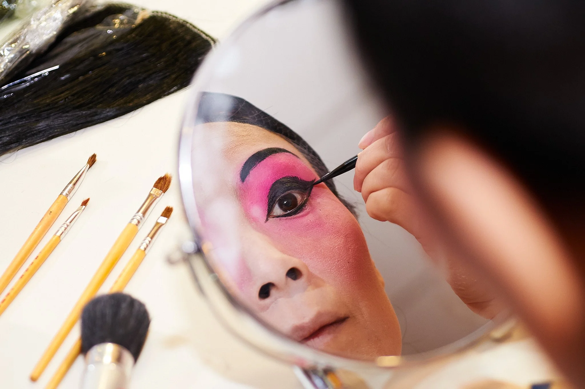 A traditional Chinese Kunqu Opera performer applying make up in a mirror before a performance in London