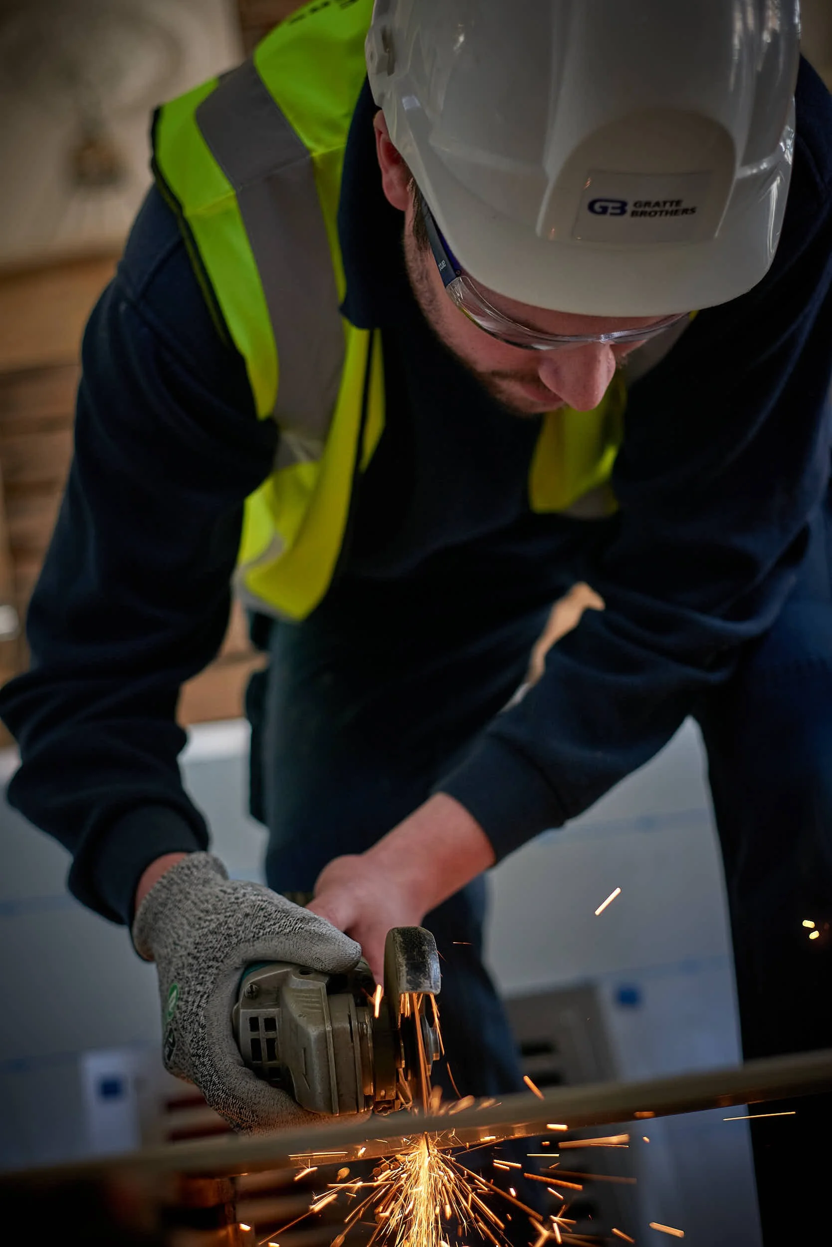 A man wearing personal protective equipment using an angle grinder on a building site