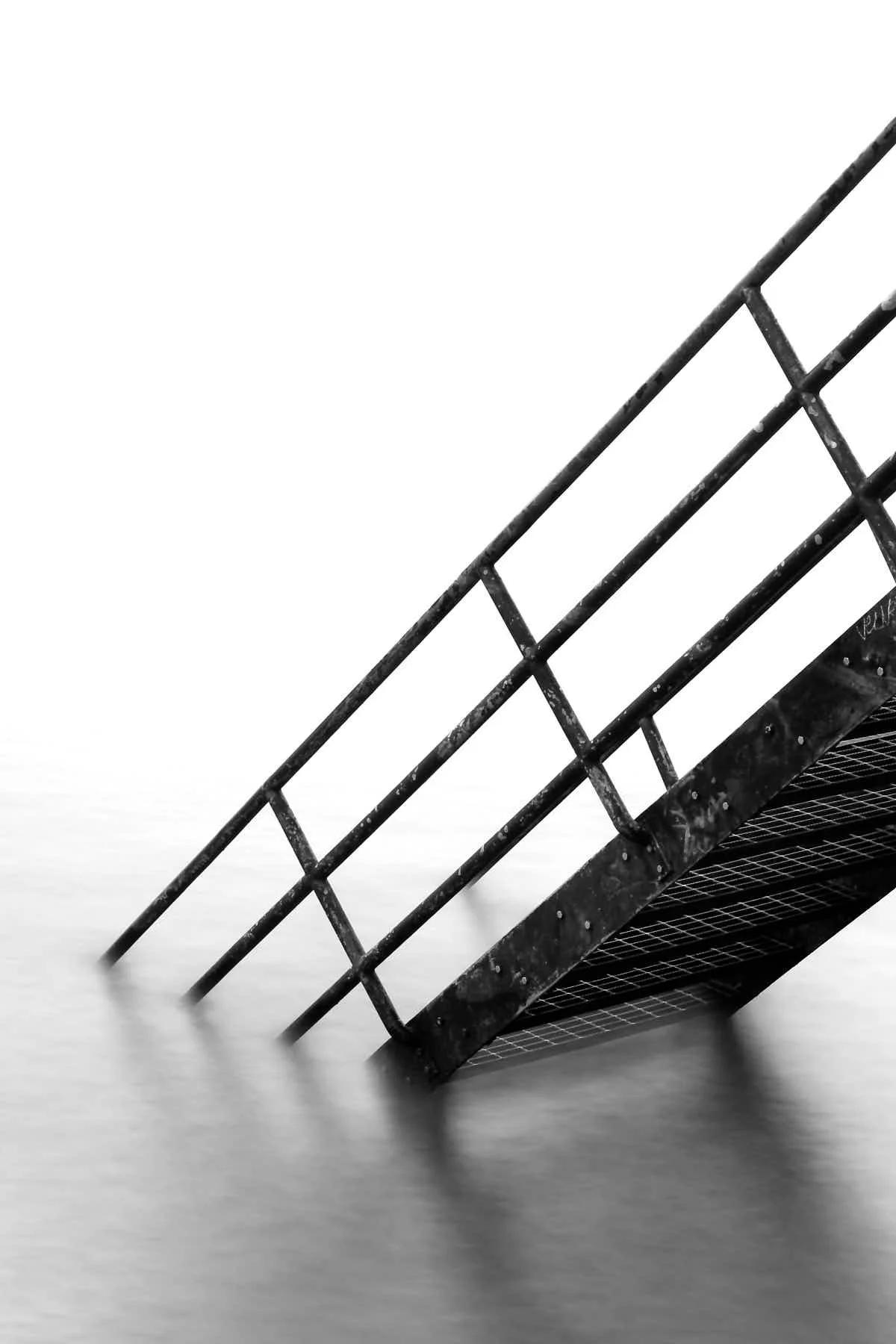 Close-up of an industrial metal staircase with a railing, seen at a tilted angle against a plain white background.