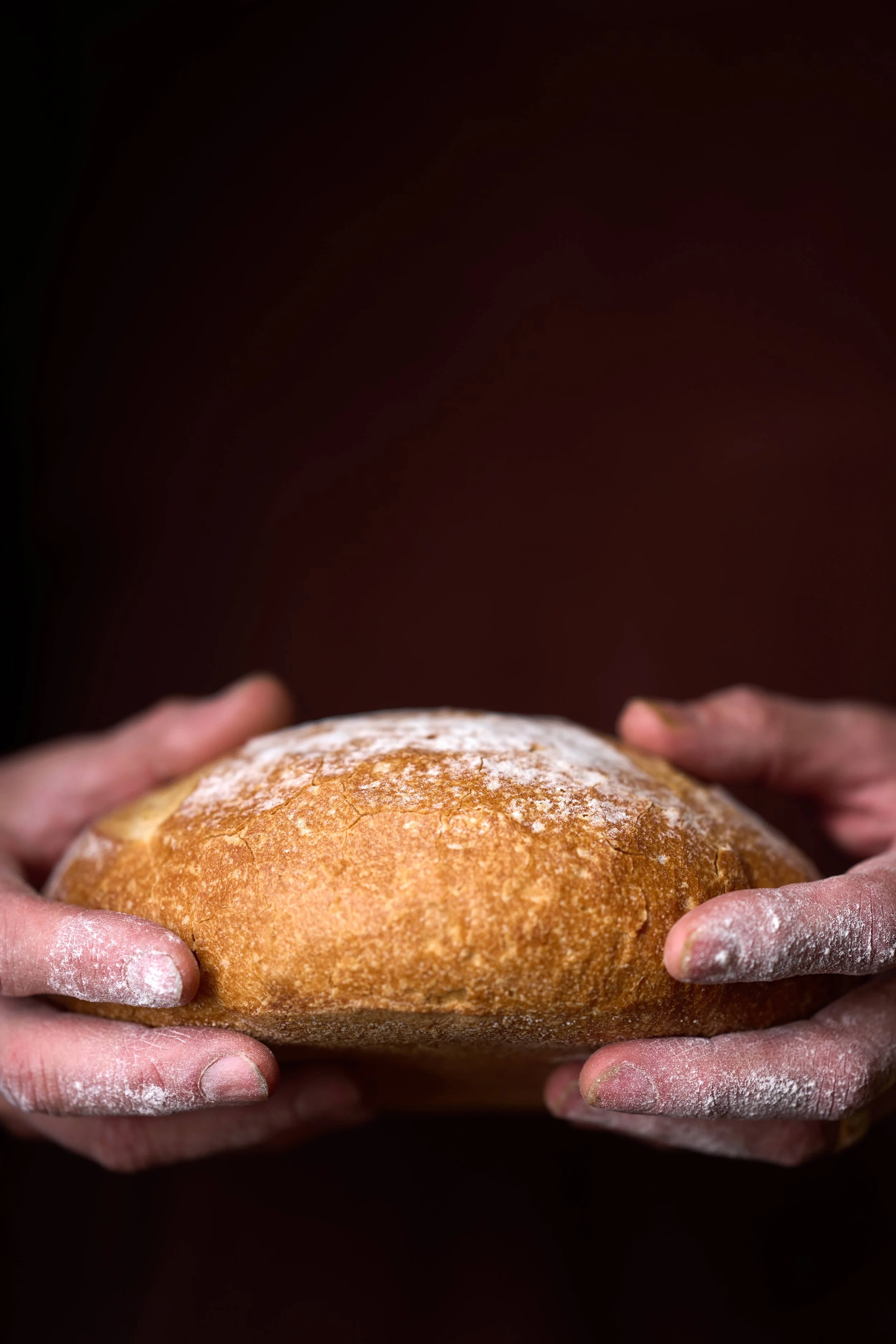 Close up of a pair of hands covered in flour holding a loaf of bread