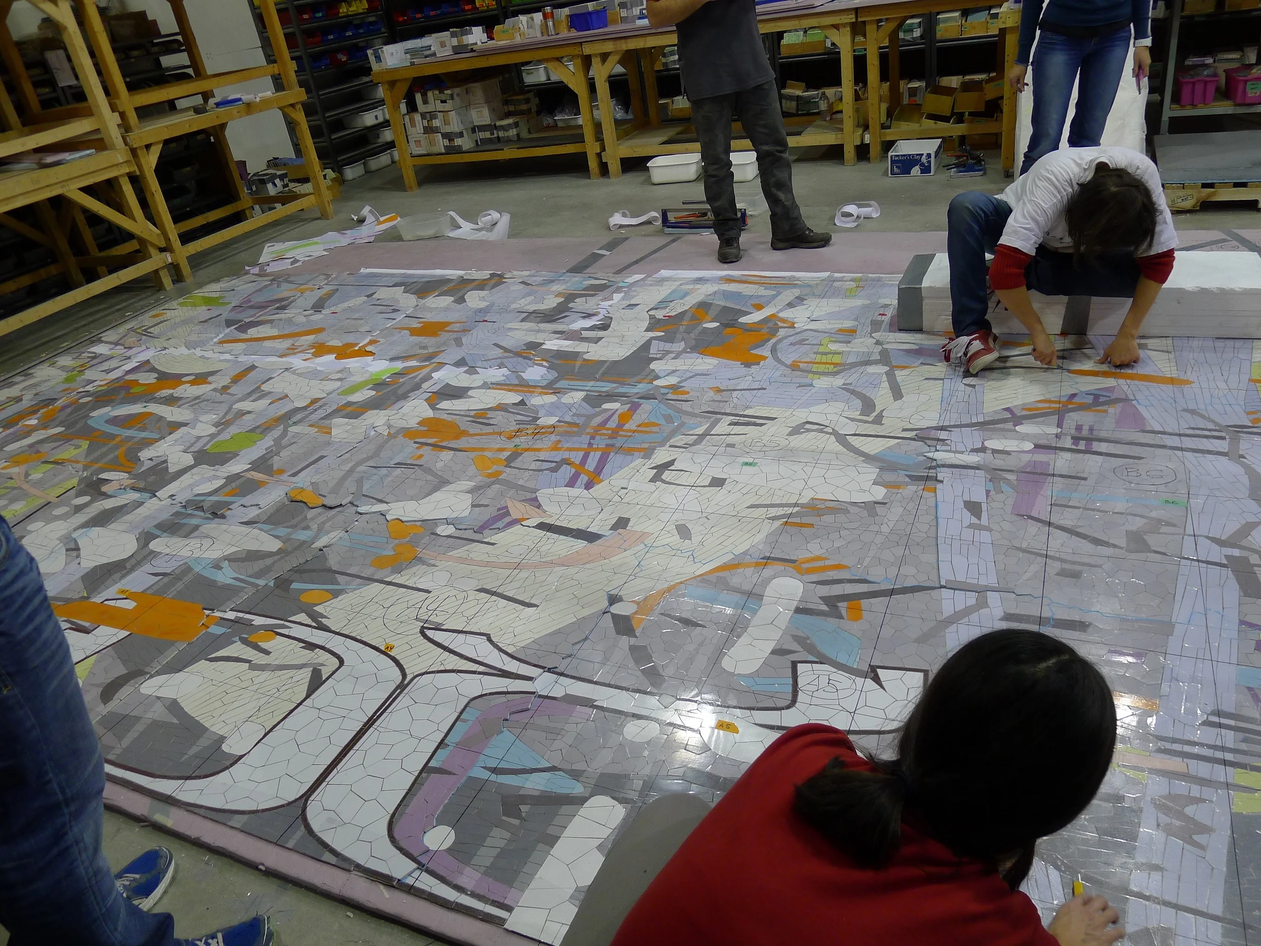 Artists seal the mosaic between two sheets of clear plastic and draw a grid onto the surface. It is then cut into smaller sections for crating and shipping.