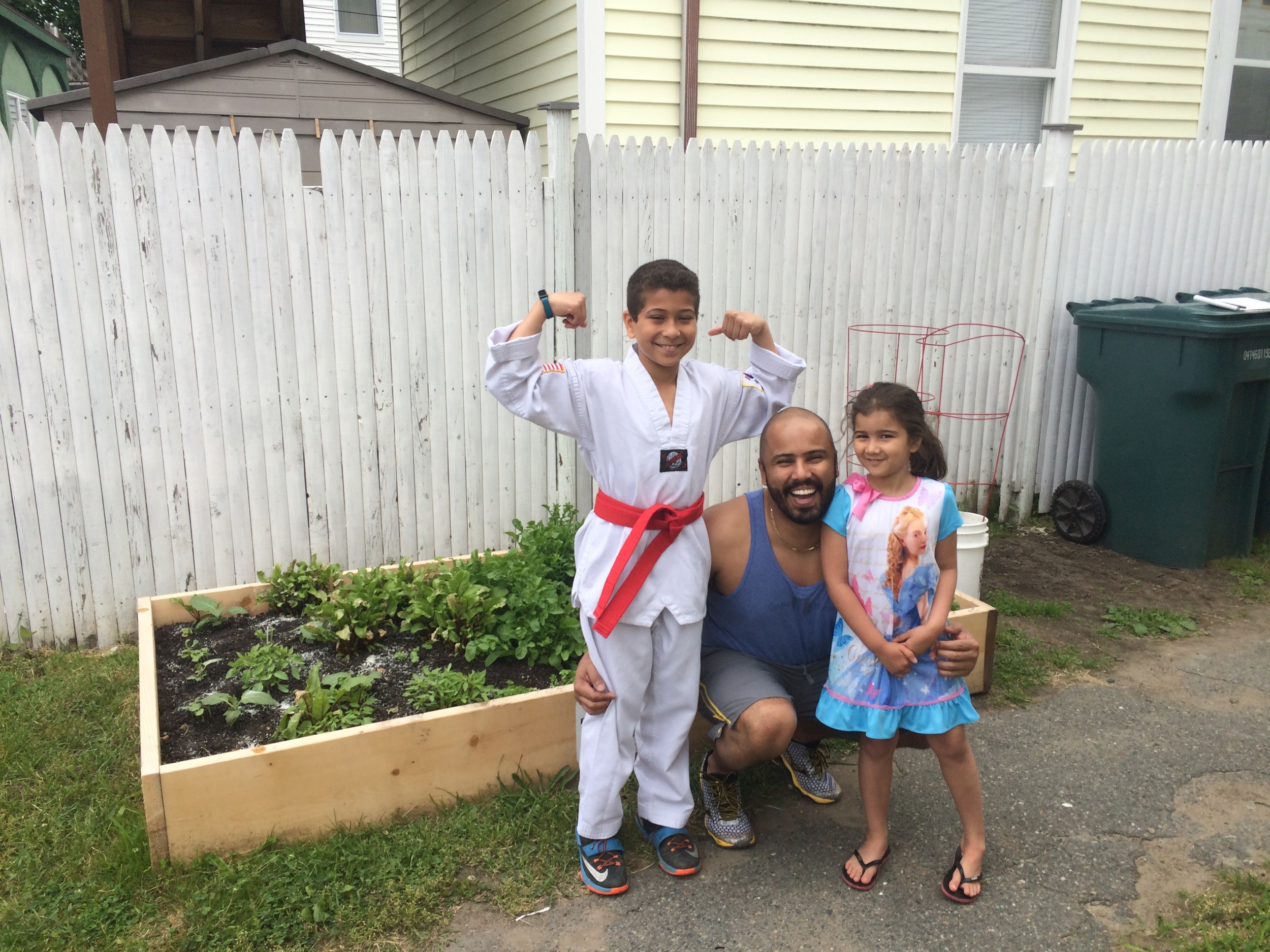Ryan, Fernando, and Sarah stand proudly in front of their garden.
