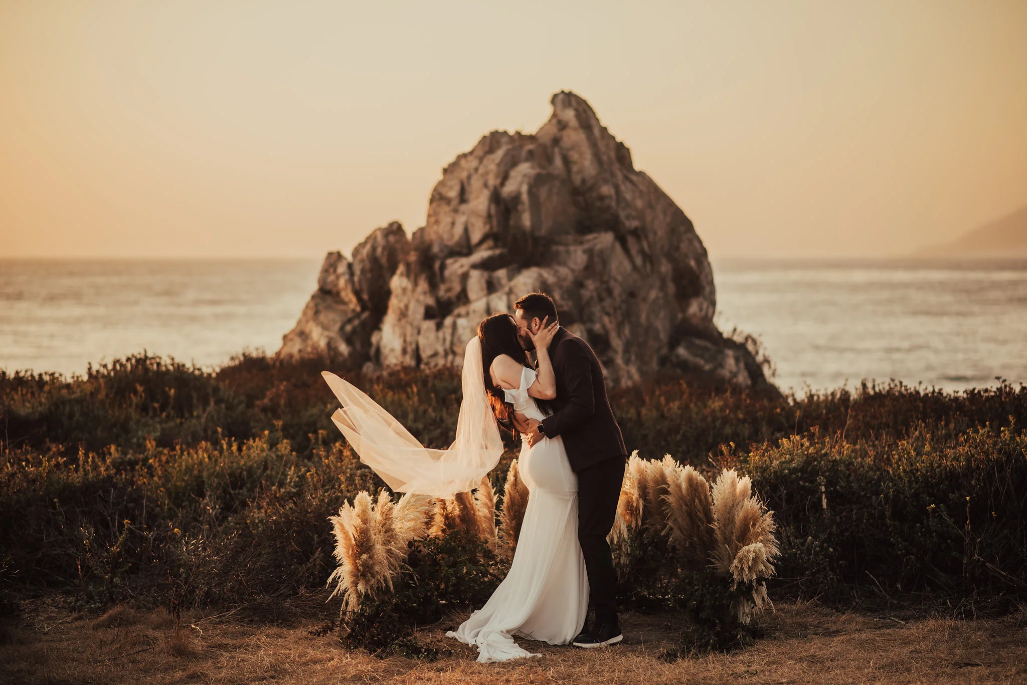 Bride with long veil shares first kiss with groom on Big Sur coast photographed by Big Sur Wedding Photographers Tessa Tadlock 