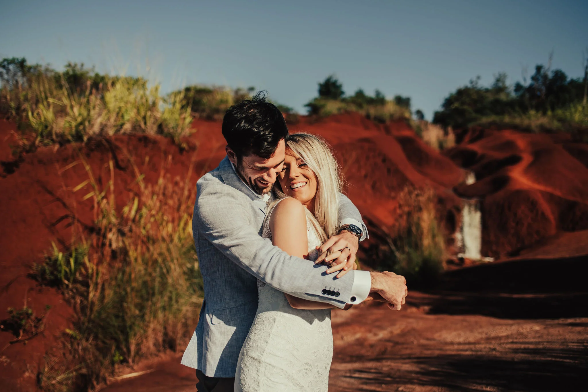 Groom Wraps Arms Around Bride for Red Cliffs Portrait Photographed by Santa Barbara Wedding Photographers Tessa Tadlock