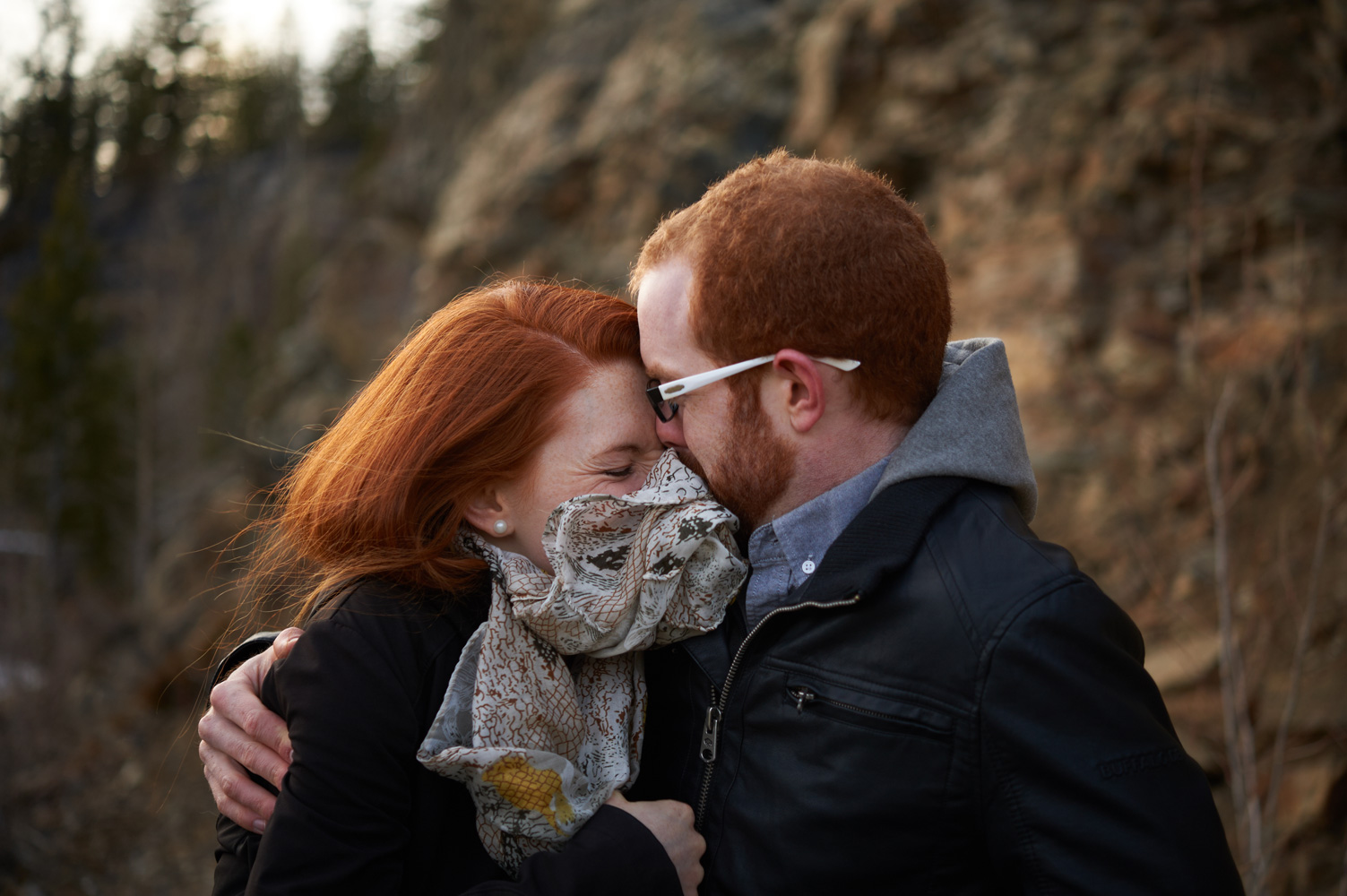 engaged-couple-snuggling-in-the-breeze-in-front-of-rock-face.jpg