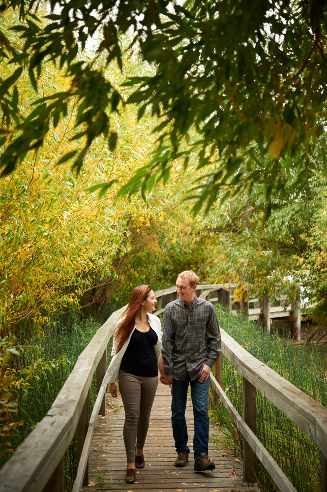 engaged-couple-walking-hand-in-hand-down-a-boardwalk-in-fall.jpg