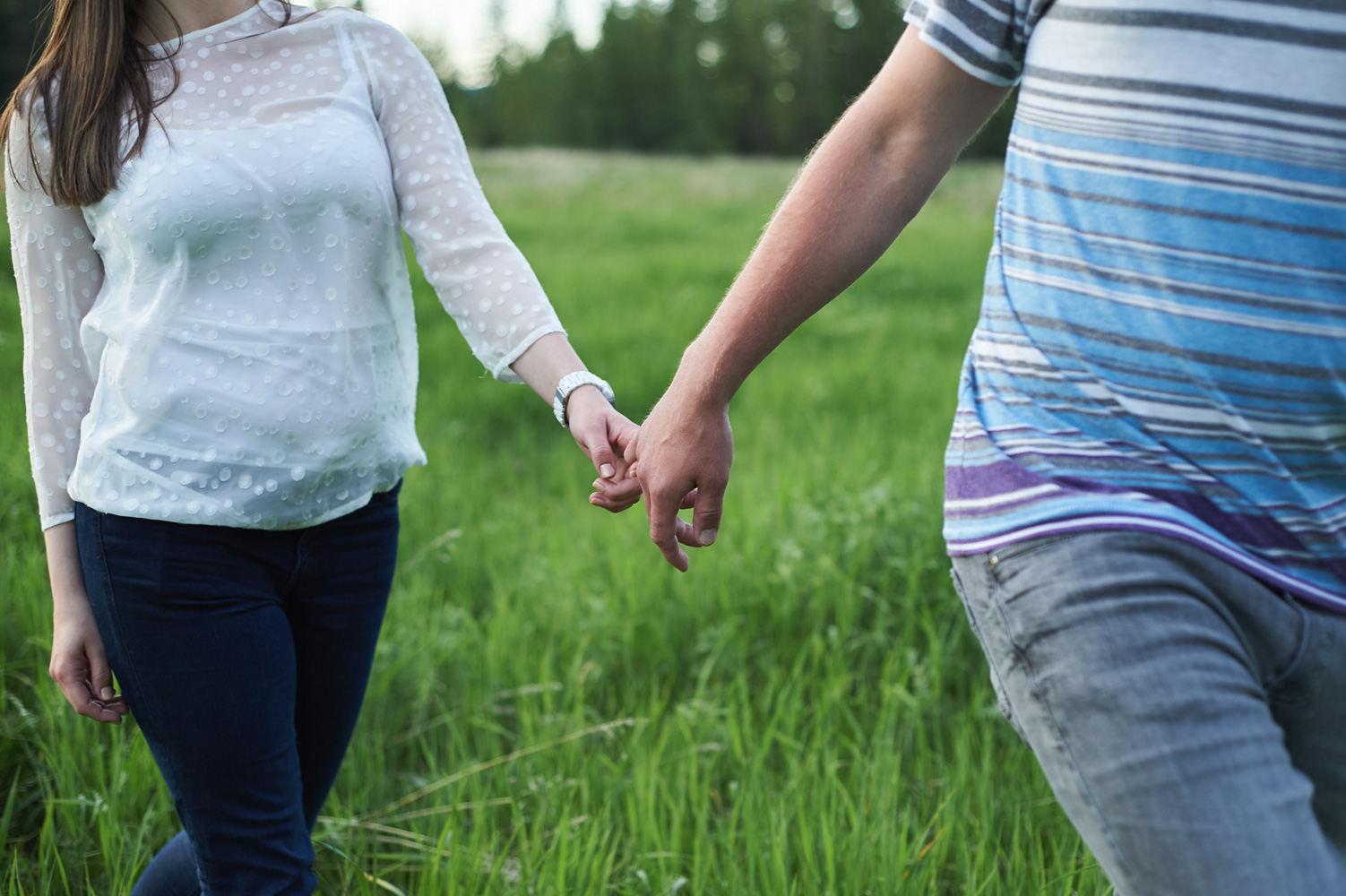 engaged-couple-walking-hand-in-hand-through-a-grassy-field.jpg