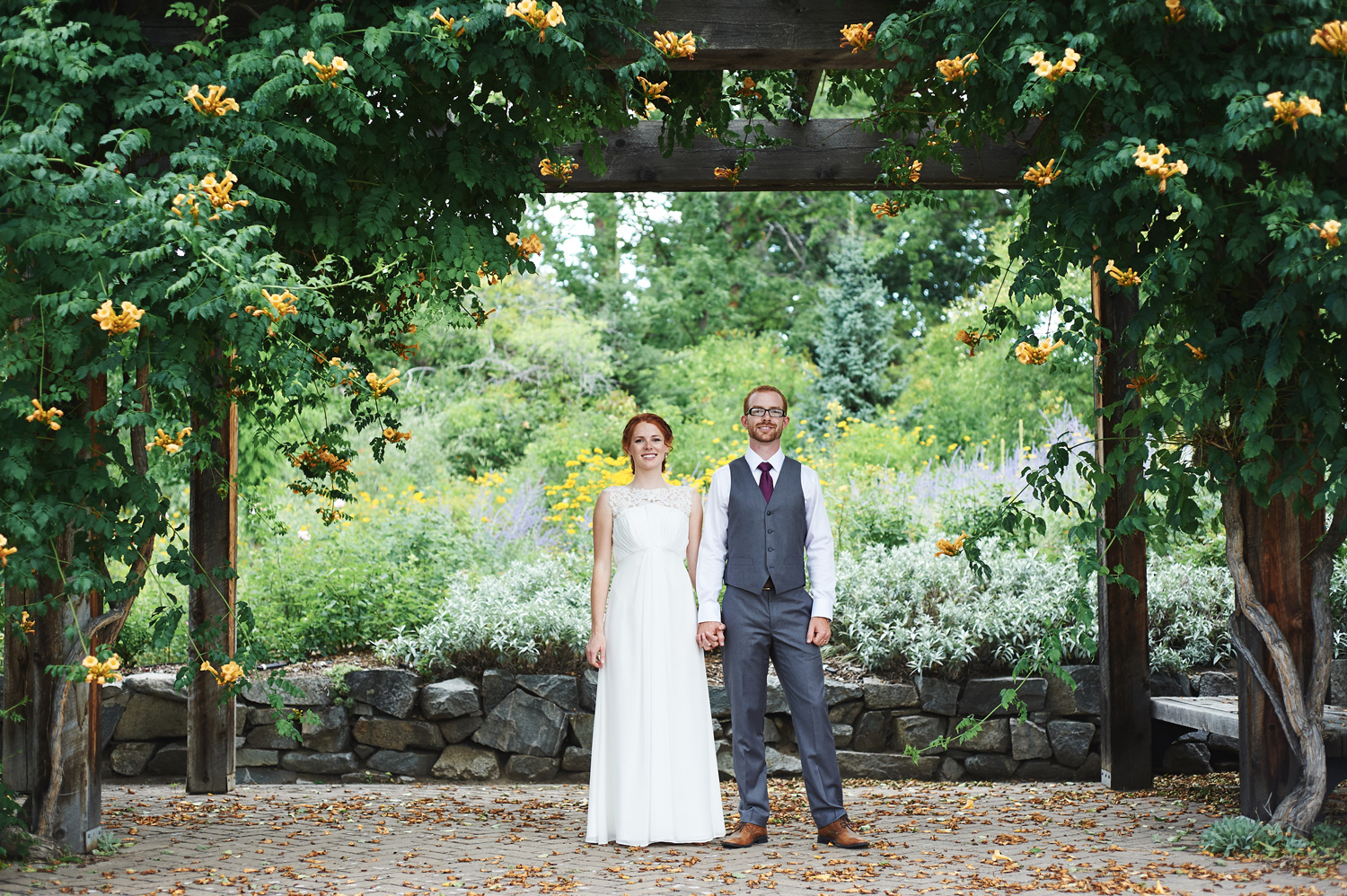 bride-and-groom-standing-hand-in-hand-under-a-wooden-trellis.jpg