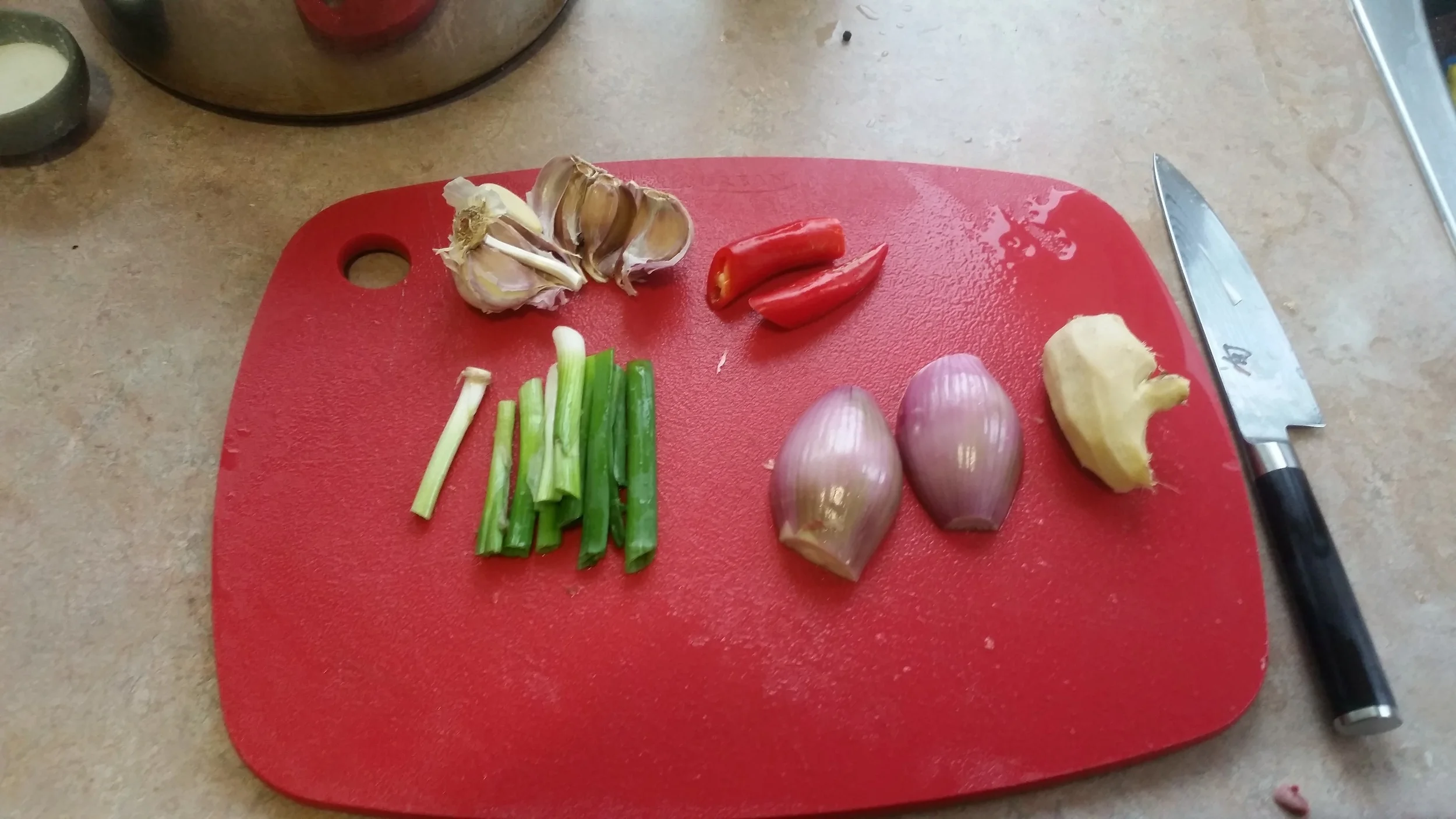 Prep your aromatics: peel and slice the shallot, discard the roots of the green onion, peel the ginger, smash the garlic.