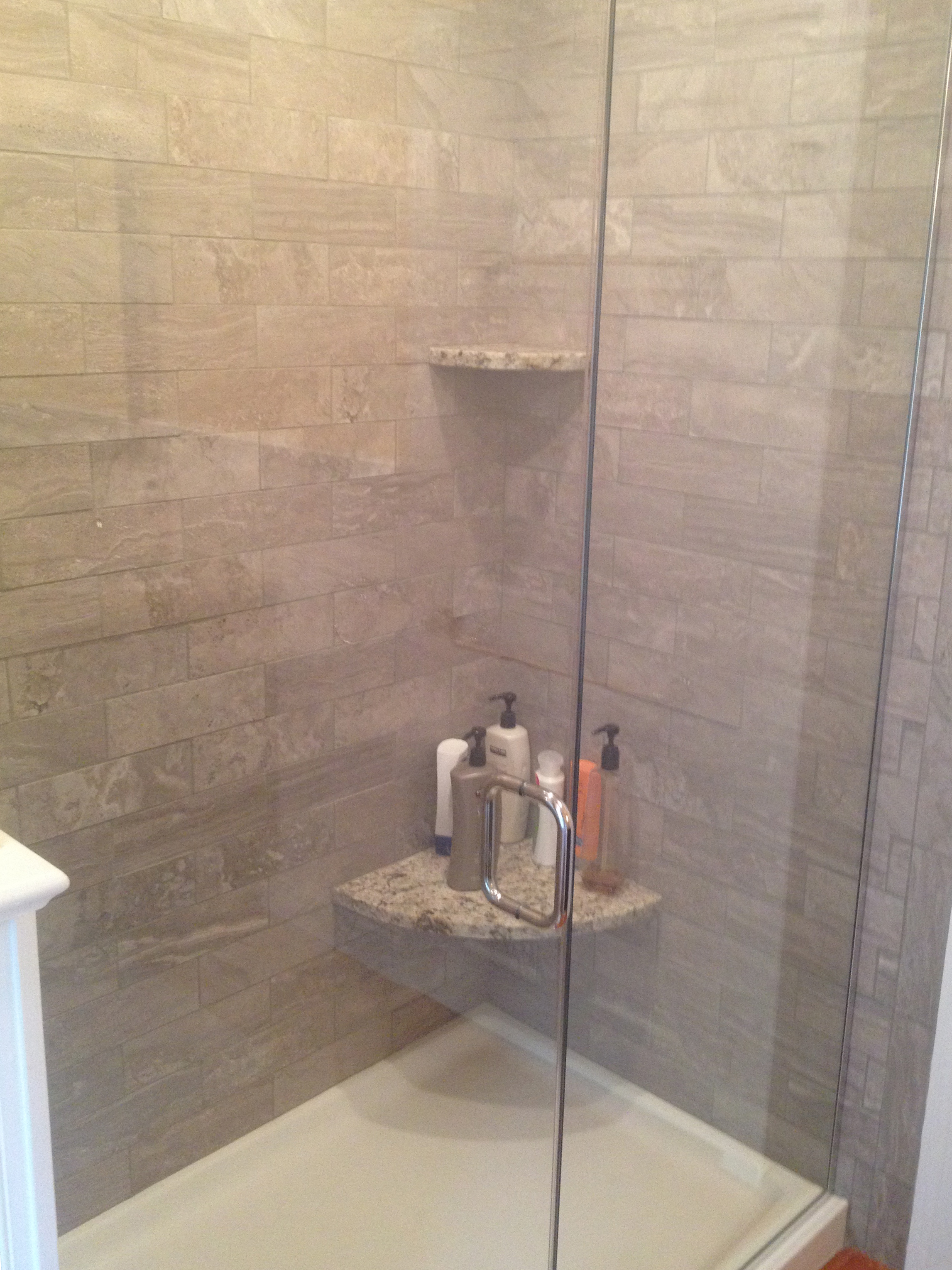  A new tile shower with a frameless glass enclosure. &nbsp;The granite seat matches the vanity countertop. 