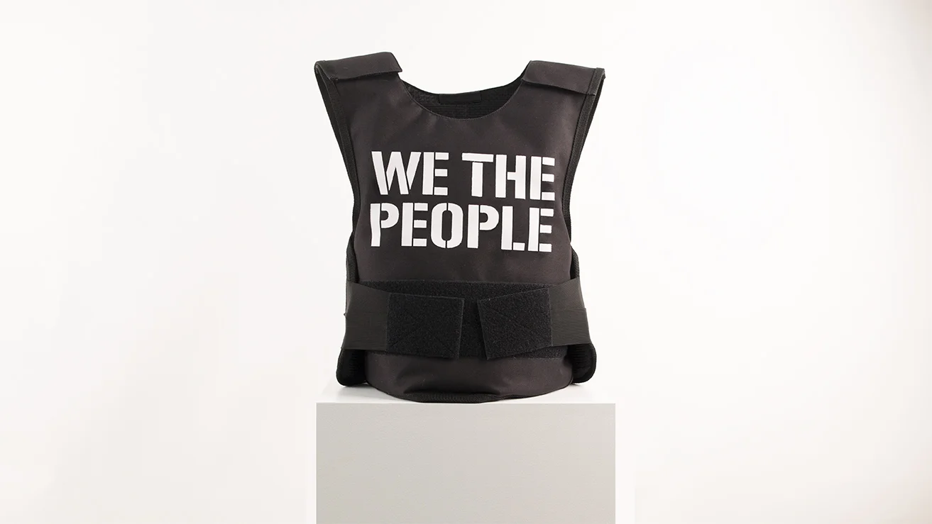 2017 Bulletproof vest, acrylic paint H60 x W10 x L16 in. “Untitled” is the new social sculpture by artist, designer, activist Sebastian Errazuriz. The piece continues his series of politically charged sculptures inspired by the dada sculptures and current social political state. Errazuriz appropriates a bulletproof vest by painting “We The People” on the front and “Civilian” on the back. The quote reminds us of civic right movements in the 60s when there was an urge for equality, social justice and humanity. The multiple recent violent events remind us that we still need to defend human rights. The act of wearing a bulletproof vest implies the acknowledgement the small but nevertheless real risk of danger that can occur when peacefully protesting. Although the vest is a peaceful tool it can be perceived as a violent object. The bulletproof vest is charged with the potential violence it defends the wearer of. The defensive piece addresses the latent danger of being a peaceful civilian in the current political state. As many works by Errazuriz, “Untitled” blurs the boundaries between art, design and activism. The vest is placed on a museum pedestal and is understood as a sculpture by the viewer. The owner can also take the piece out of its art context and wear a work that can save his life. The stencil font used to write “We The People” and “Civilian” reminds us of improvised mass production aesthetic. The stencil’s design is downloadable for free on the artist’s website to encourage the masses to replicate and defend themselves peacefully.