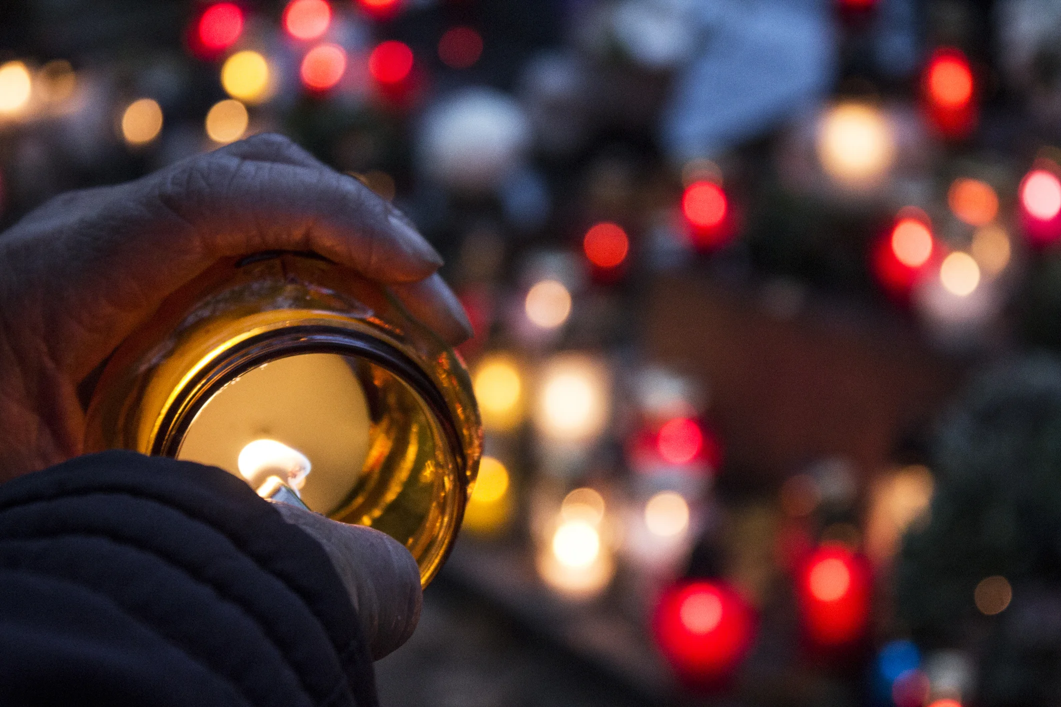 Focused nighttime image of hand lighting a candle during a vigil amongst a bokeh of candlelights. This image represents Civil Rights legislation.