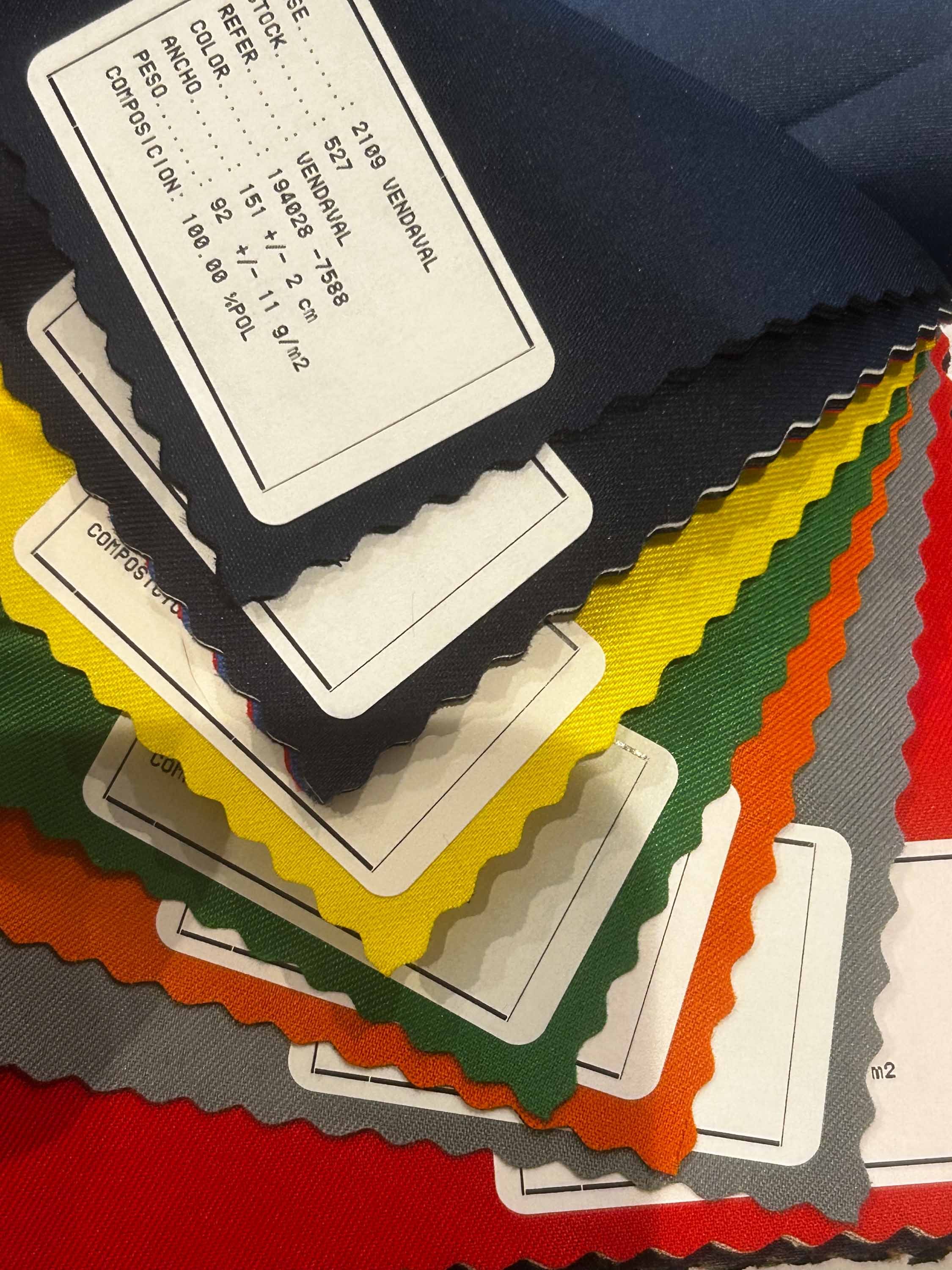 Sample fabric swatches in multiple colors including black, yellow, green, orange, gray, and red, with a close-up focus on the black swatch's tag showing fabric details.